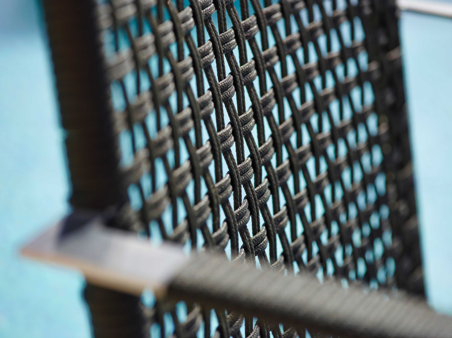 Detailaufnahme des Cane-Line "Straw" Outdoor Armlehnstuhls mit geflochtener Sitzfläche und Armlehne.