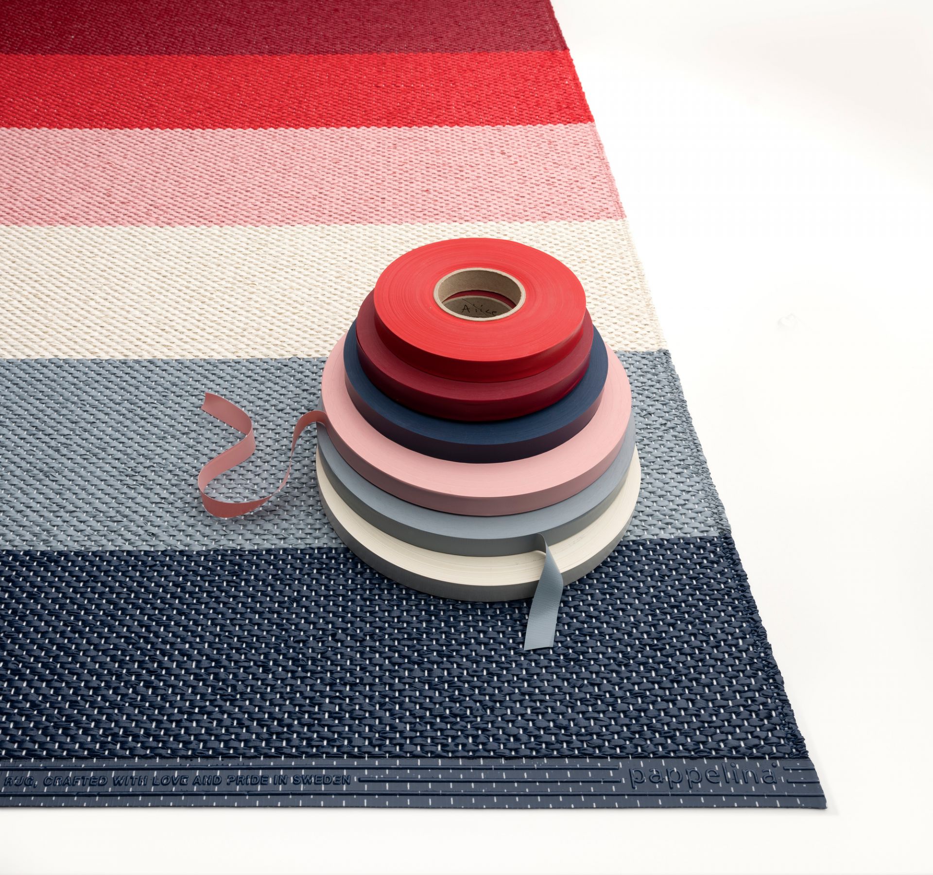 Pappelina Molly Kunststoffteppich mit bunten Streifen und farblich passenden Kunststoffbändern. Robuster Teppich für Innen und Außen.