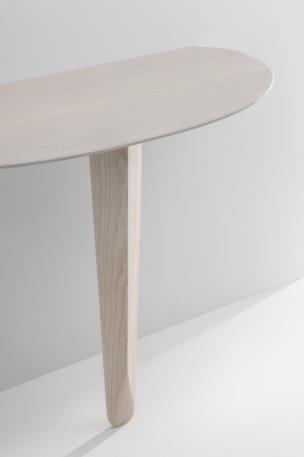 Detailaufnahme des Kuyu Konsolentischs: Ovale Tischplatte und ein Bein aus hellem Holz.