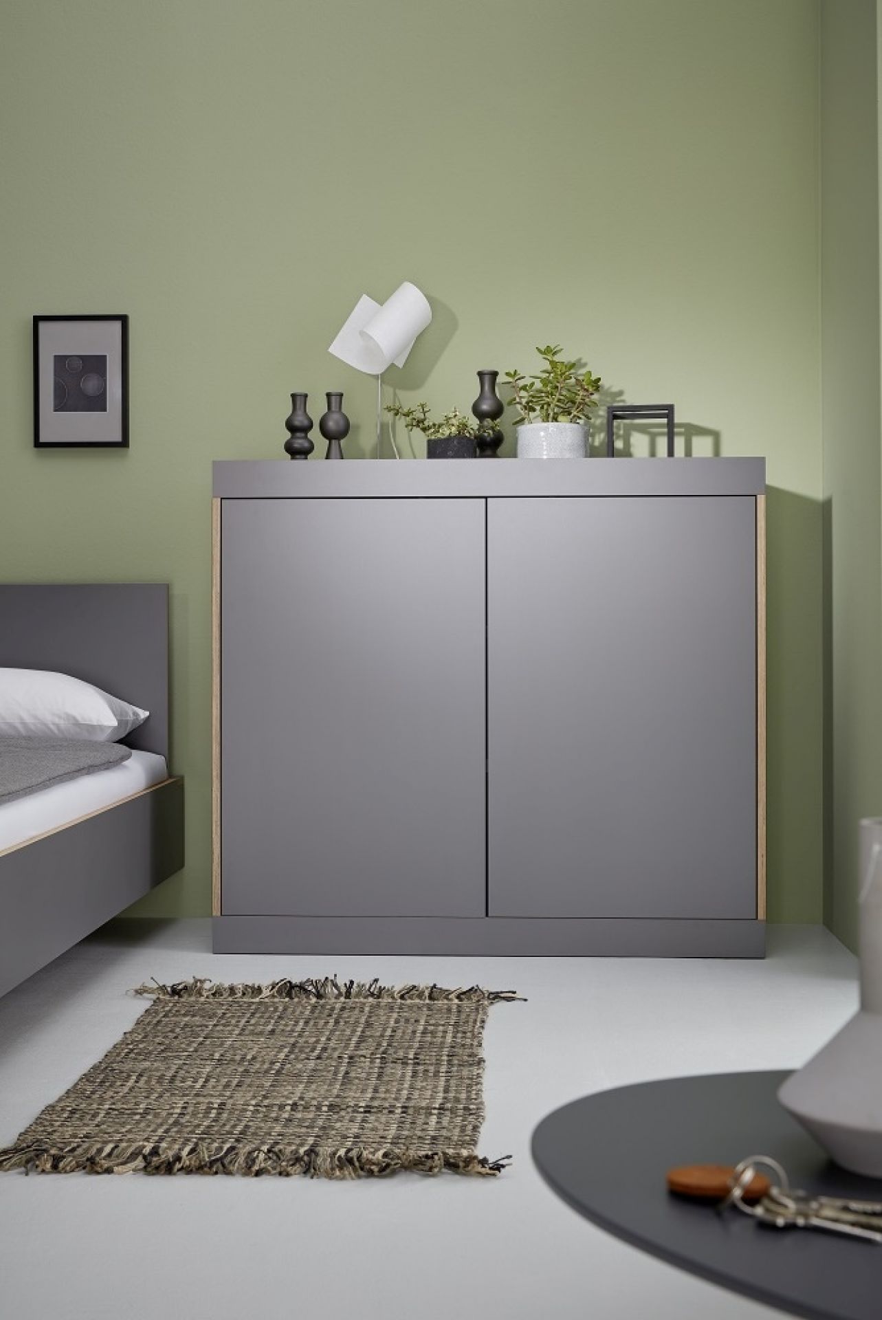 Graue Flai Kommode von Müller Möbelwerkstätten im Schlafzimmer mit Deko und Teppich.
