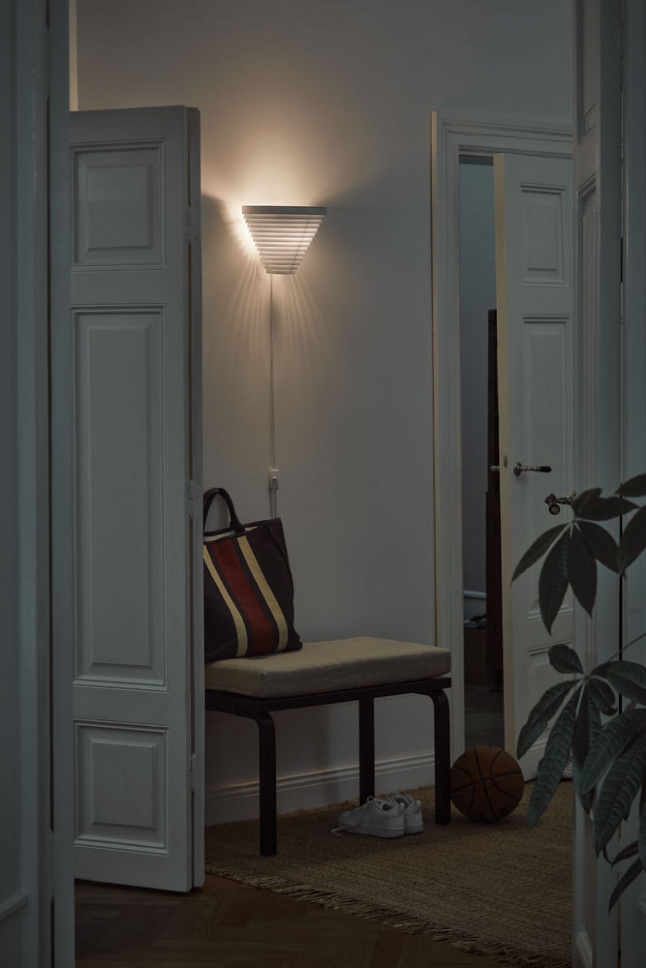 Artek A910 Wandleuchte in einem Flur, neben einer Bank mit Tasche und Schuhen.