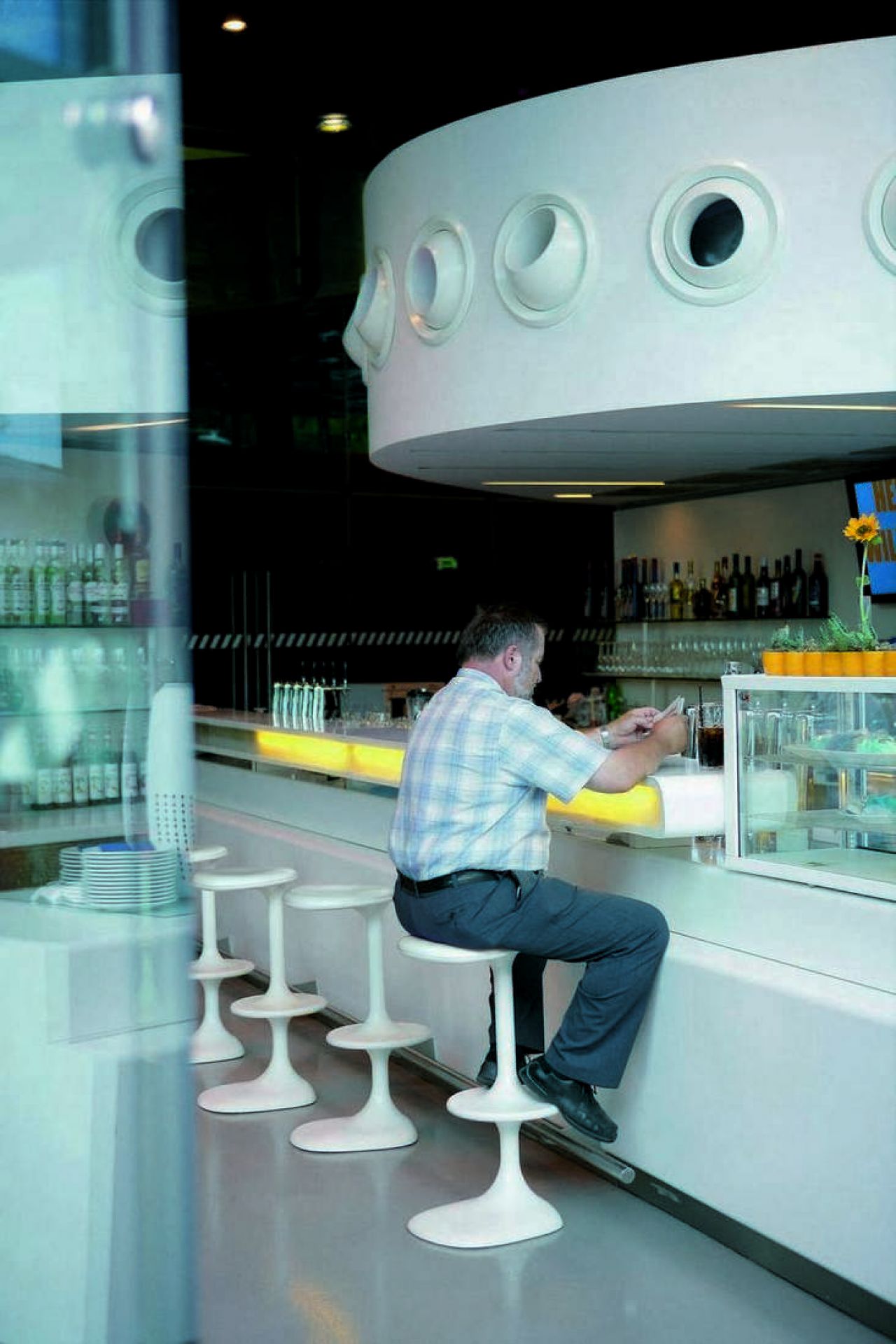 Mann sitzt auf einem weißen Kant Barhocker von Casamania Horm an einer Bar.