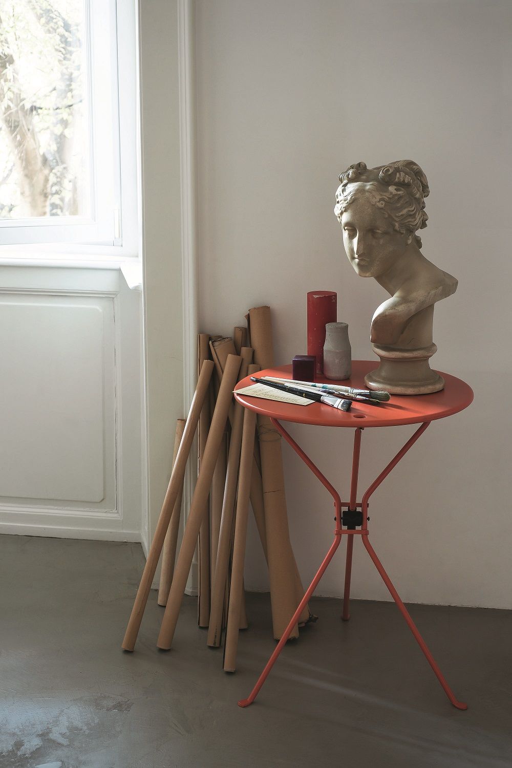 Oranger Cumano Klapptisch von Zanotta mit Büste und Malutensilien in einem hellen Raum.