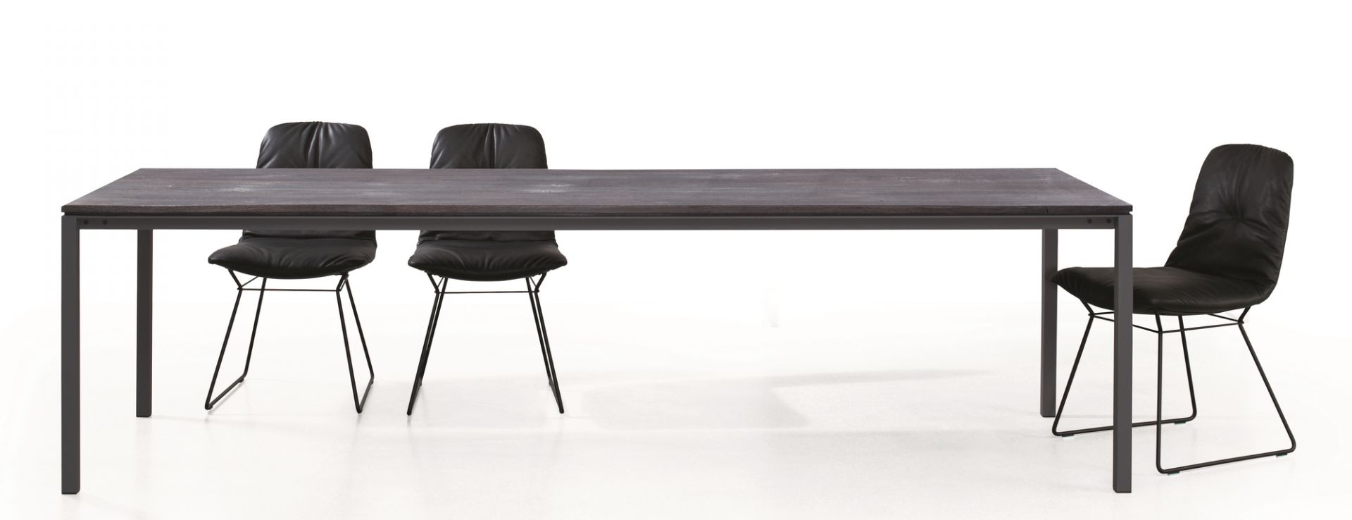 S 600 Tisch von Janua: Esstisch aus geköhlter Eiche mit schwarzen Stühlen auf weißem Hintergrund.