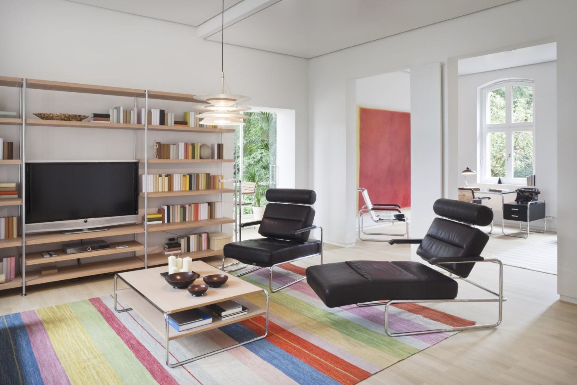 Wohnzimmer mit Thonet Couchtisch B 20 b/1, Fachboden, Bücherregal, Sessel und farbigem Teppich.