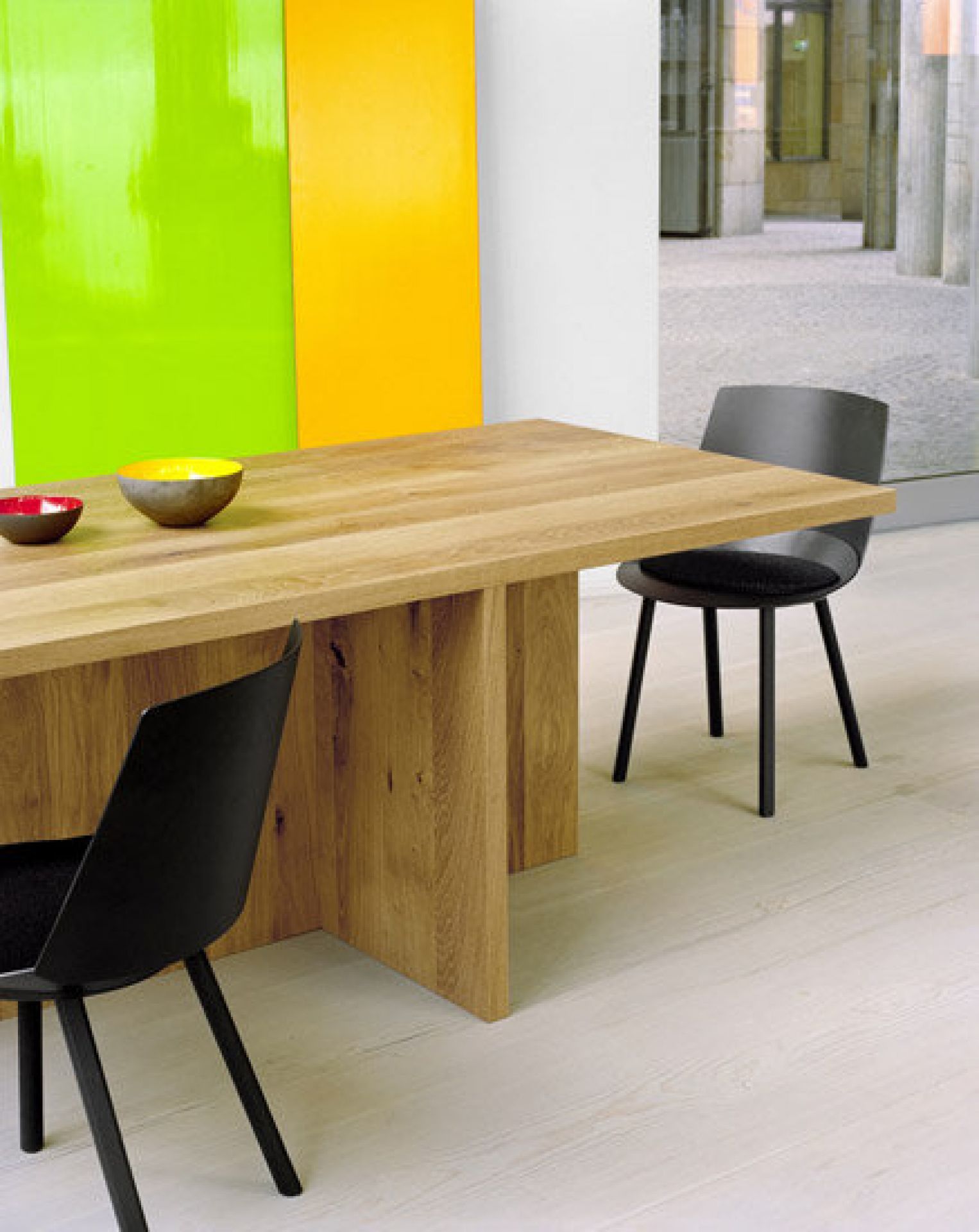 TA18 Esstisch von e15: Massiver Holztisch mit zwei schwarzen Stühlen und farbigen Schalen.