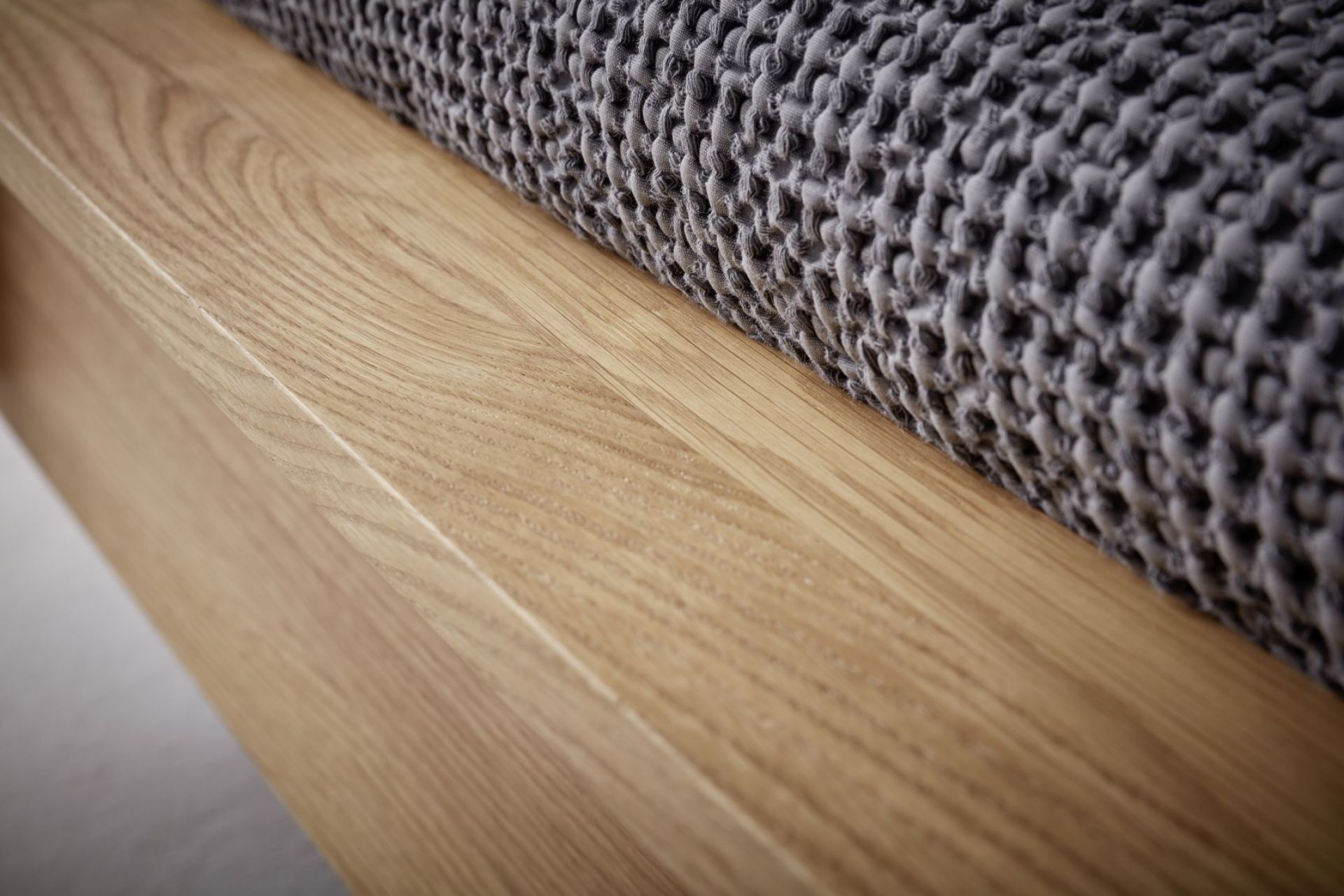 Detailaufnahme: Flai Doppelbett Eiche von Müller Möbelwerkstätten mit grauer Tagesdecke. Massivholz Bettrahmen mit natürlicher Holzmaserung.
