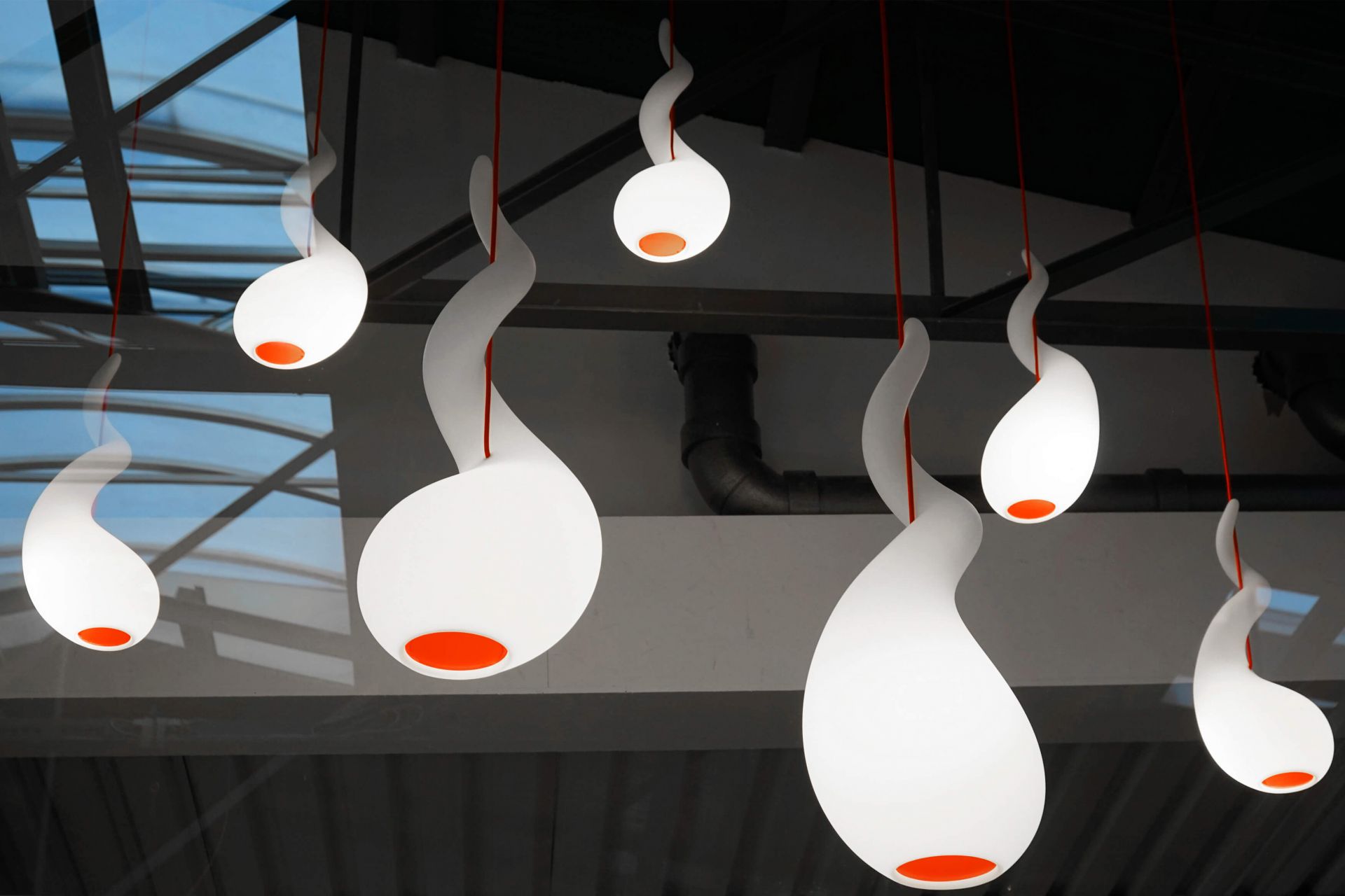 Mehrere Alien PL Pendelleuchten Next mit geschwungenem Design und roter Akzentfarbe hängen von der Decke.