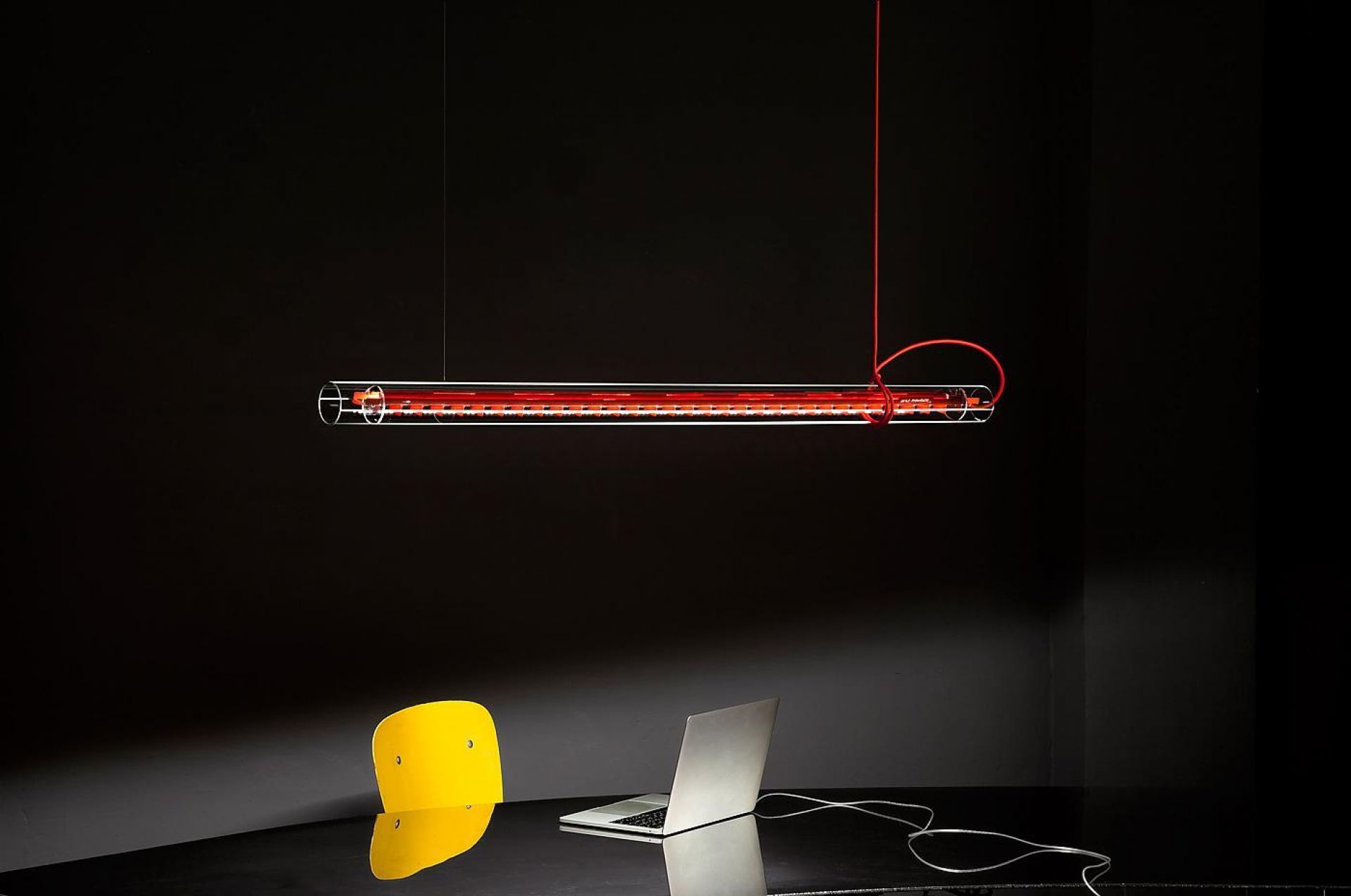 Tubular LED Hängeleuchte von Ingo Maurer mit rotem Kabel über Schreibtisch mit Laptop.
