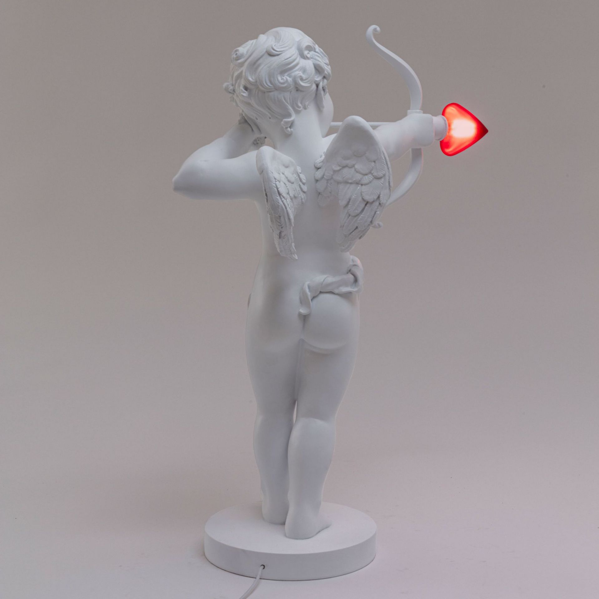 Rückansicht der weißen Seletti Cupid Lampe mit leuchtendem Herz-Pfeil. Tischleuchte für Valentinstag.