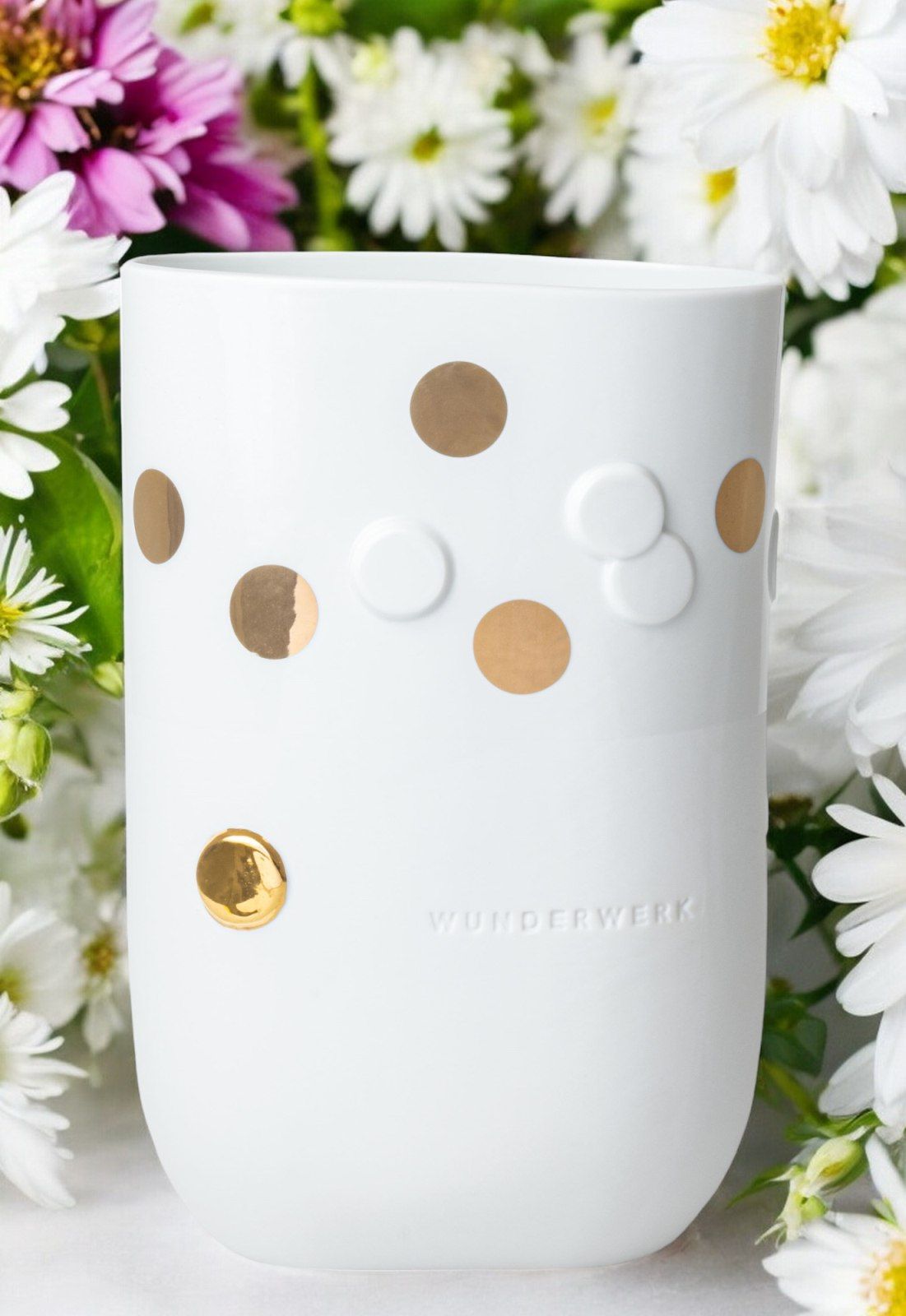 Weiße Wunderwerk Vase mit goldenen Punkten und Räder-Design, umgeben von Blumen.