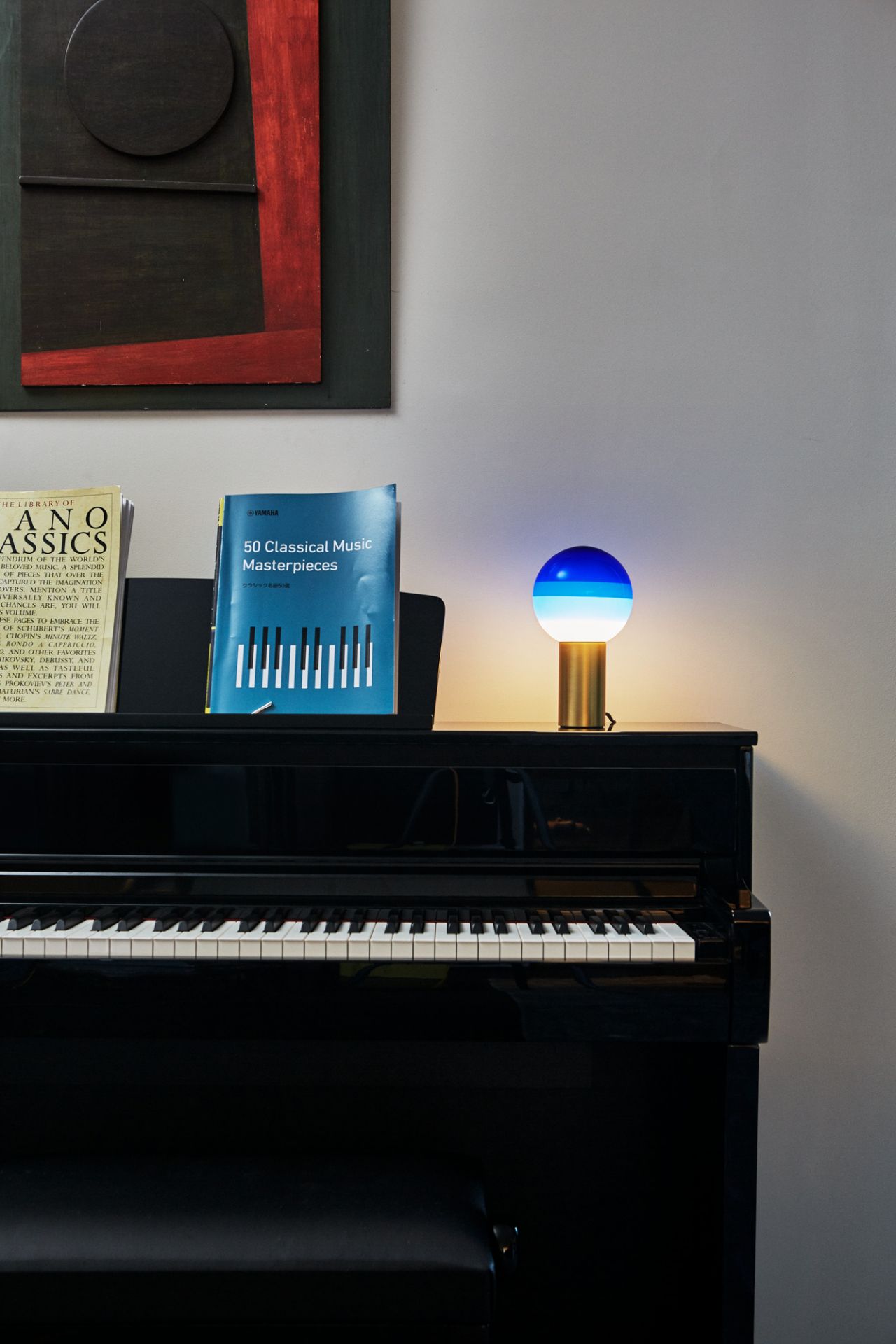 Marset Dipping Light M LED Tischleuchte mit blauem Schirm und Messingfuß auf Klavier.