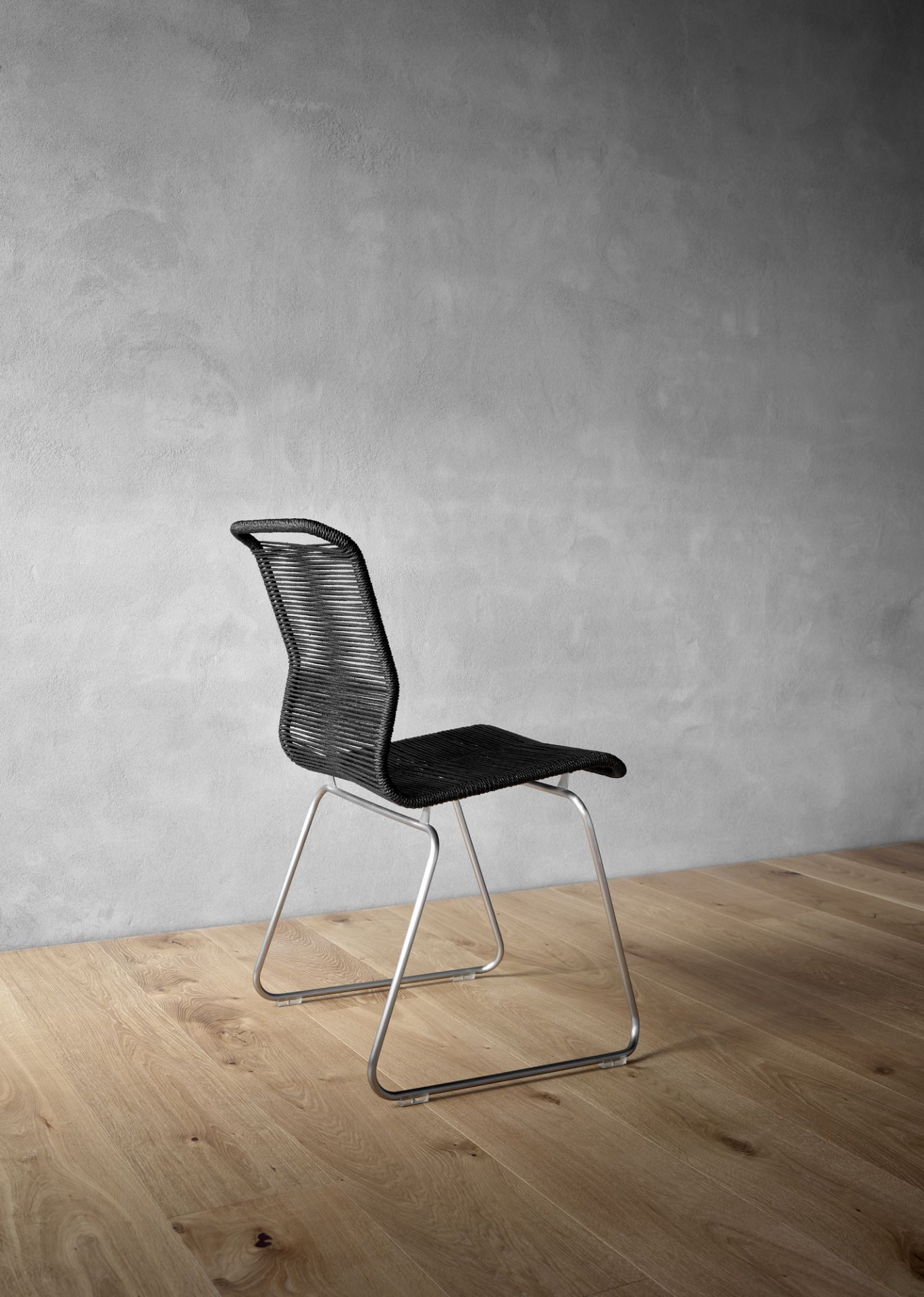 Panton One Outdoor Stuhl in Schwarz mit Edelstahlgestell auf Holzboden vor grauer Wand.