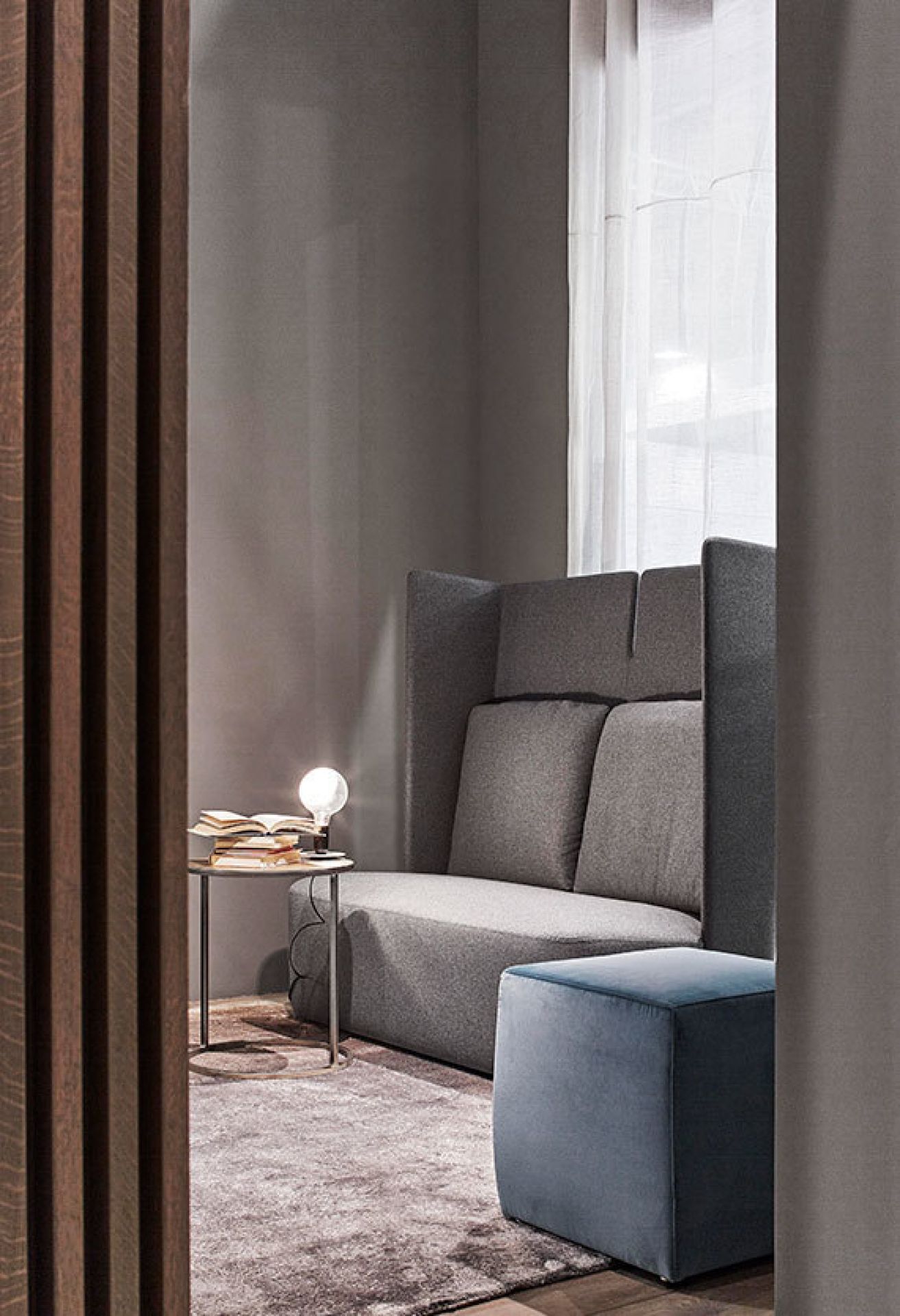 Weiße Flos Lampadina LED Tischleuchte auf Beistelltisch neben grauer Couch und blauem Hocker.