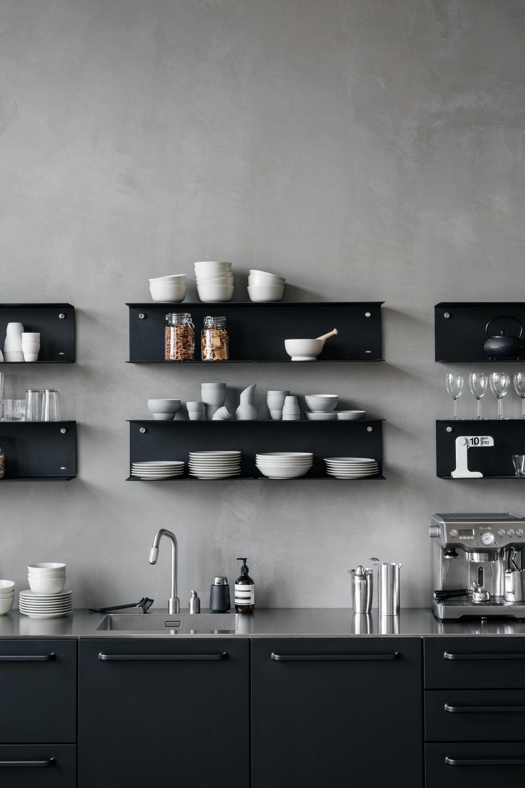 Schwarze U-Form Wandregale von Vipp an grauer Wand mit Geschirr und Küchenutensilien, modernes Küchendesign.