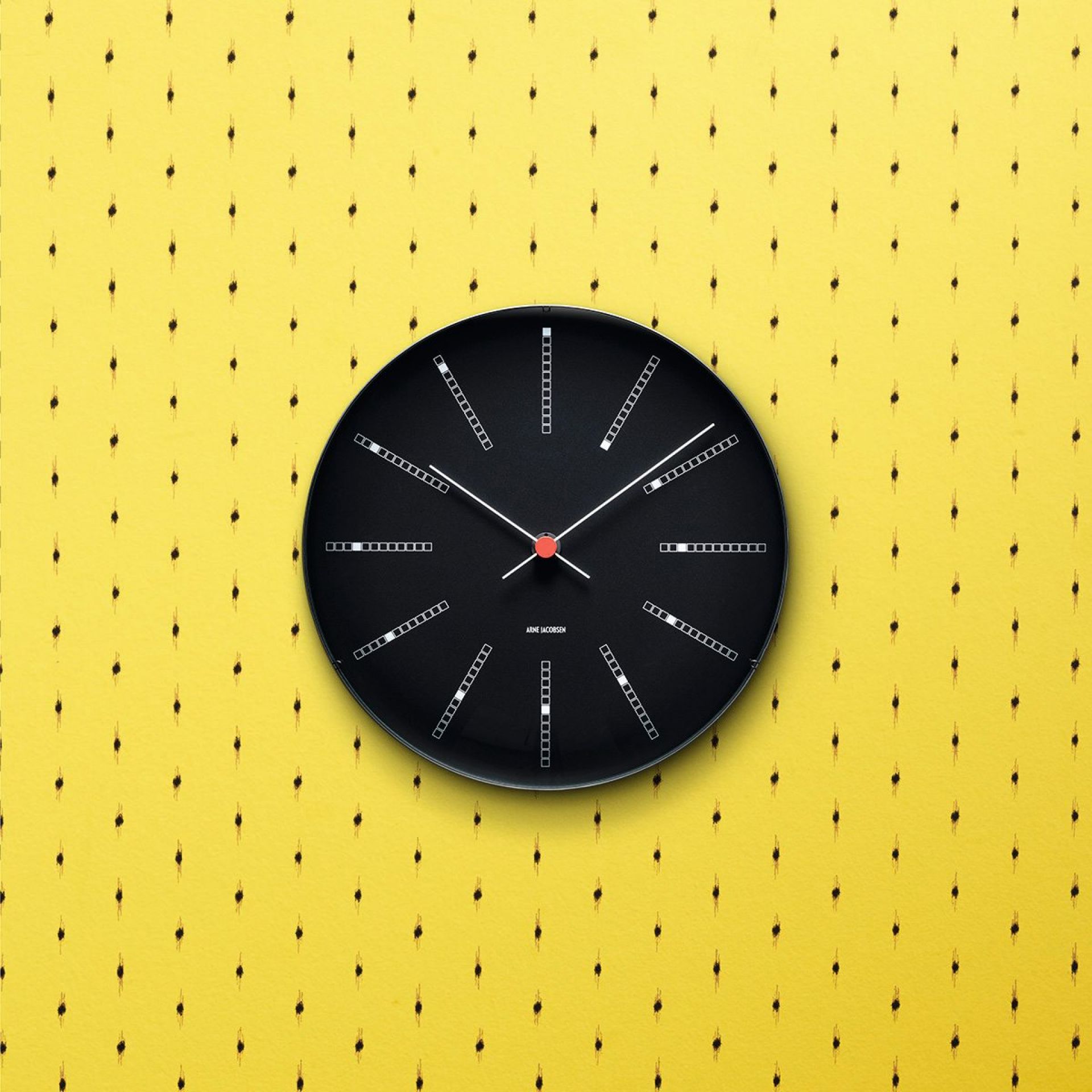 Schwarze Bankers Wanduhr von Rosendahl Timepieces, Durchmesser 21 cm, vor gelbem Hintergrund. Designuhr für Wohnzimmer und Büro.