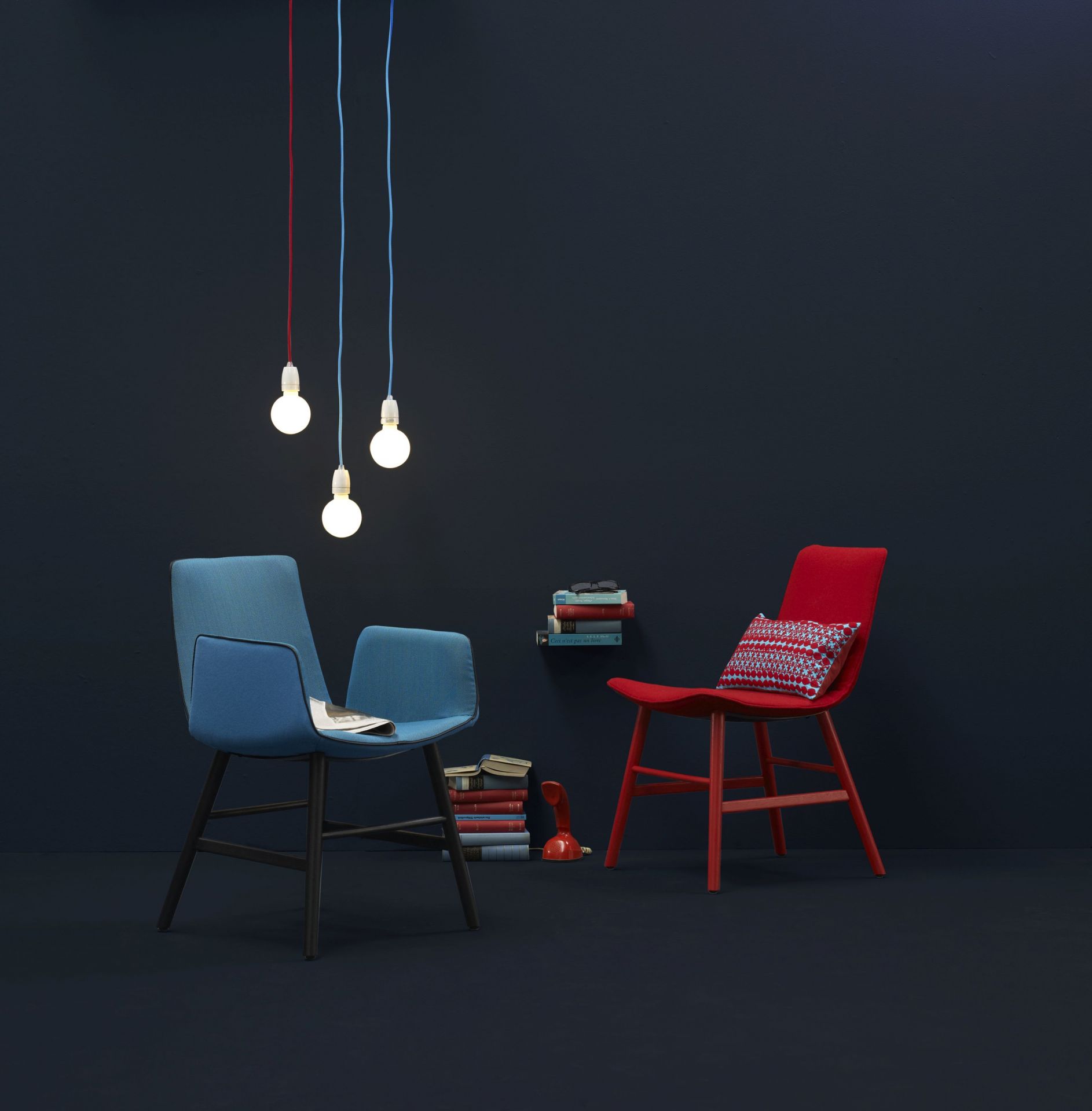 Blauer Amelie Armlehnstuhl von Freifrau Manufaktur mit hohen Armlehnen und roter Stuhl im Interieur.