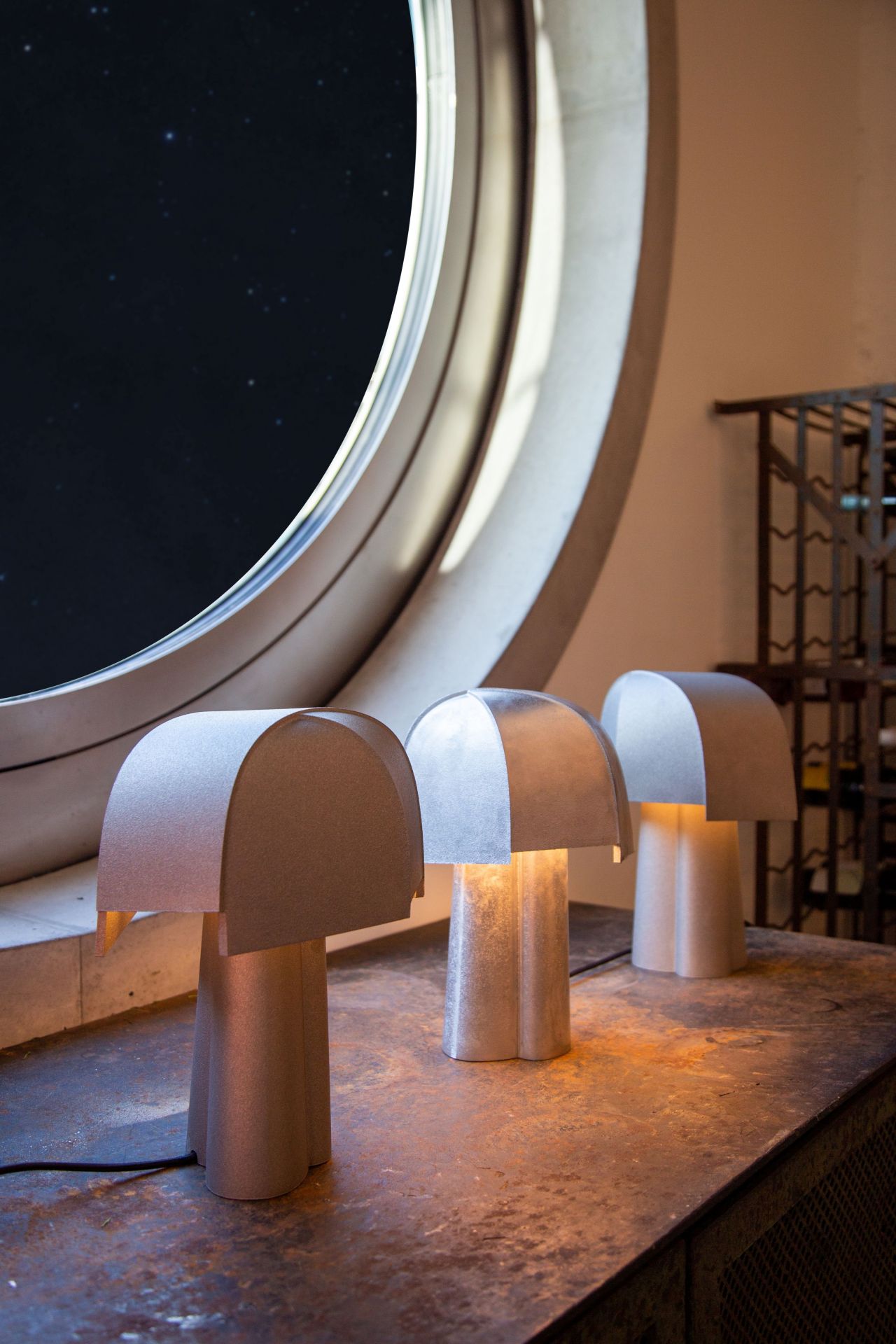 Drei Samsa Tischleuchten von Pulpo in Silber vor einem runden Fenster mit Sternenhimmel.