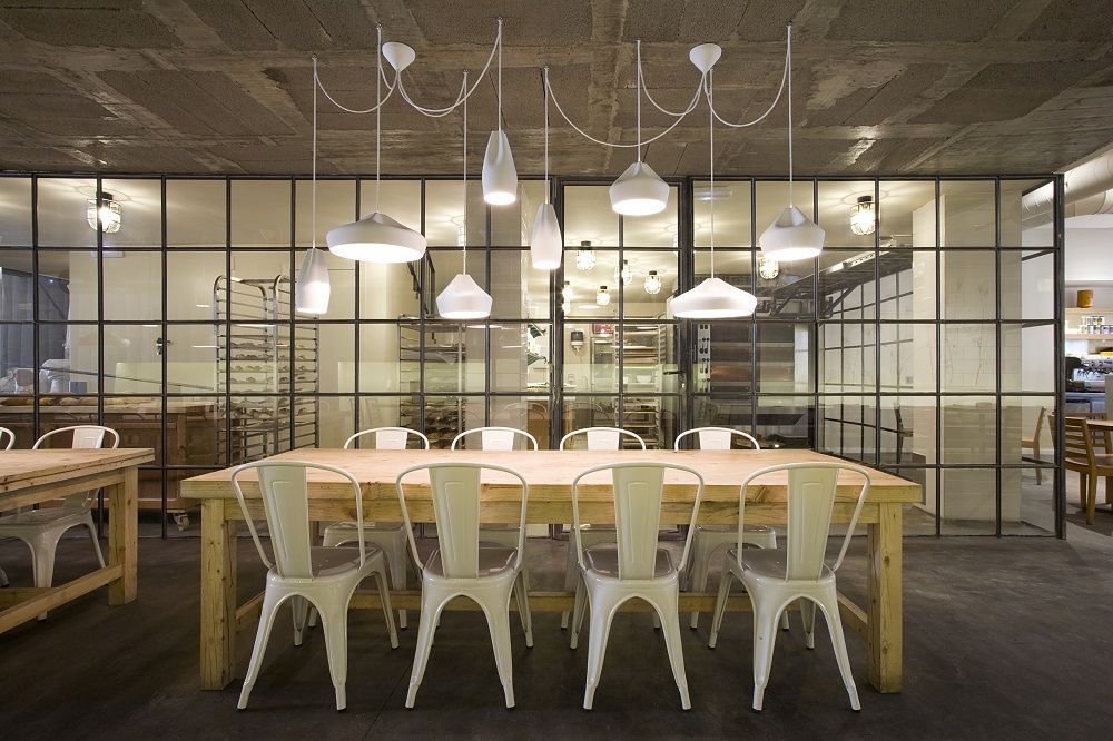 Essbereich mit mehreren weißen Pleat Box Pendelleuchten von Marset über einem langen Holztisch.