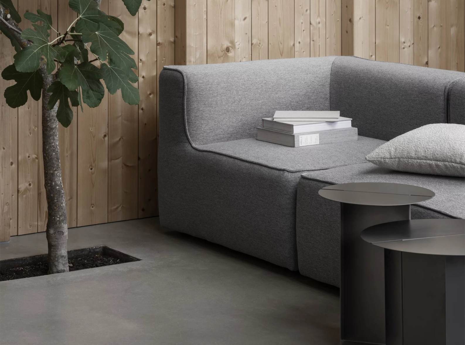 Oru Beistelltisch von Blomus, Ø 50 cm, H 40 cm, in dunklem Metall neben grauem Sofa.