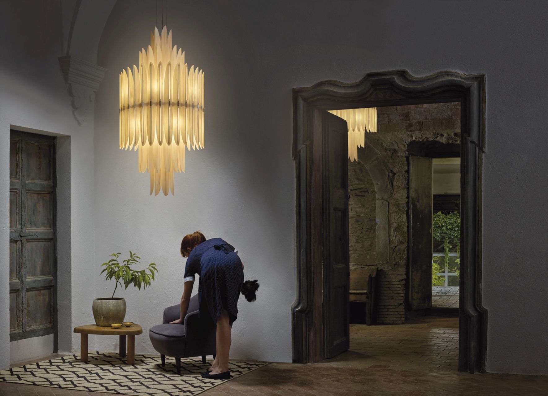 Elegante Voliere Pendelleuchte von LZF Lamps im Raum mit Frau beim Staubwischen des Sessels.