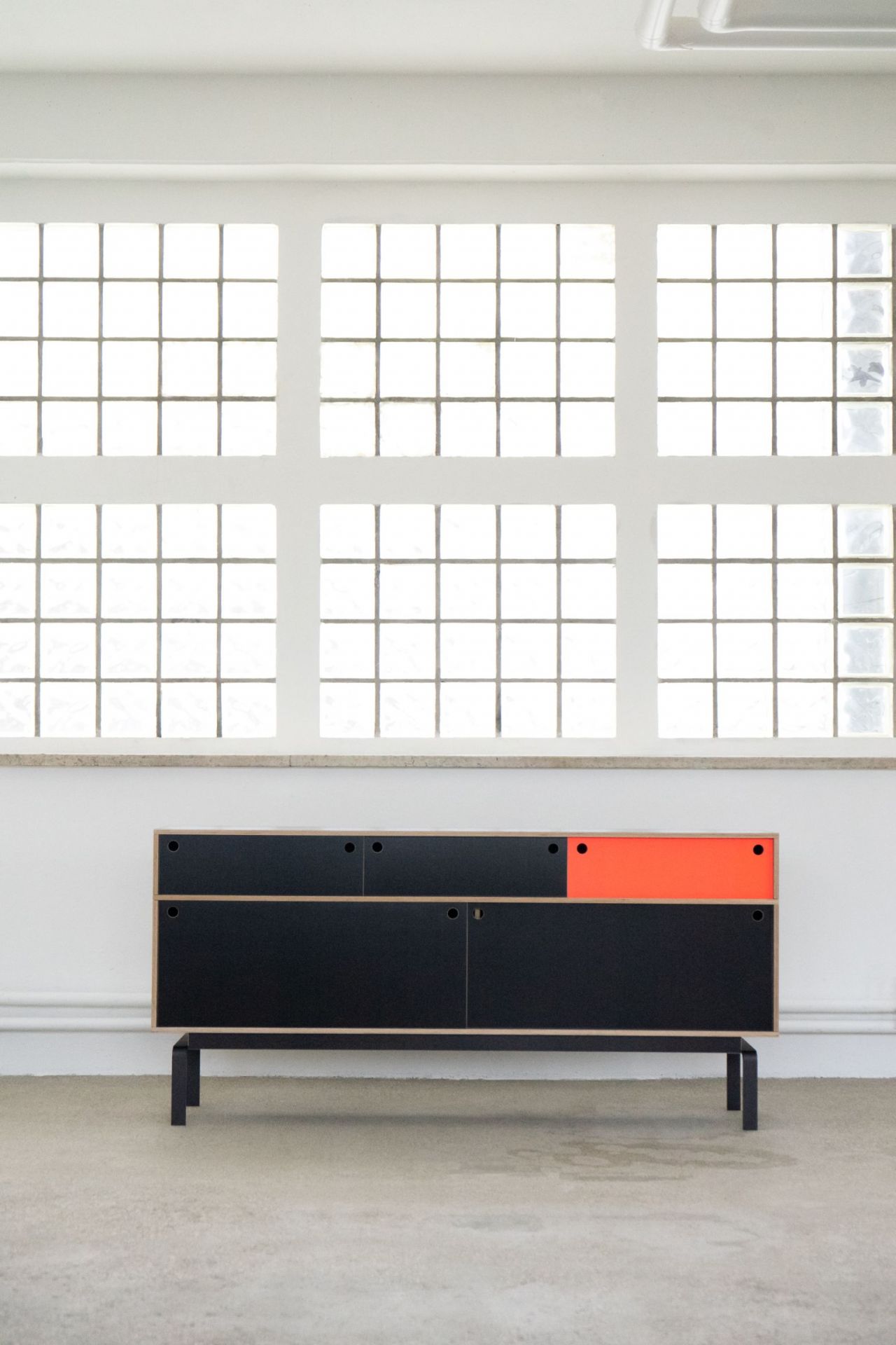 Egal Sideboard von Nils Holger Moormann: Schwarzes Sideboard mit orangefarbenem Element vor Fenster. Modernes Möbeldesign.