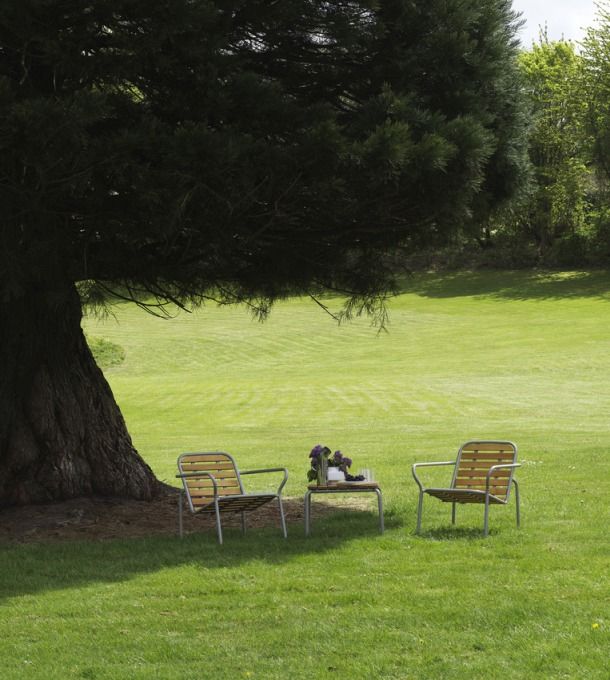 Zwei Vig Lounge Sessel aus Holz von Normann Copenhagen im Garten unter einem Baum.