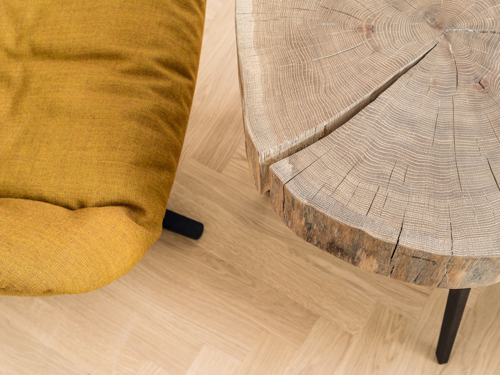 Nahaufnahme des Janua Stomp Beistelltisches H28 aus rohem Holz mit Baumscheiben-Optik neben einem gelben Sessel.