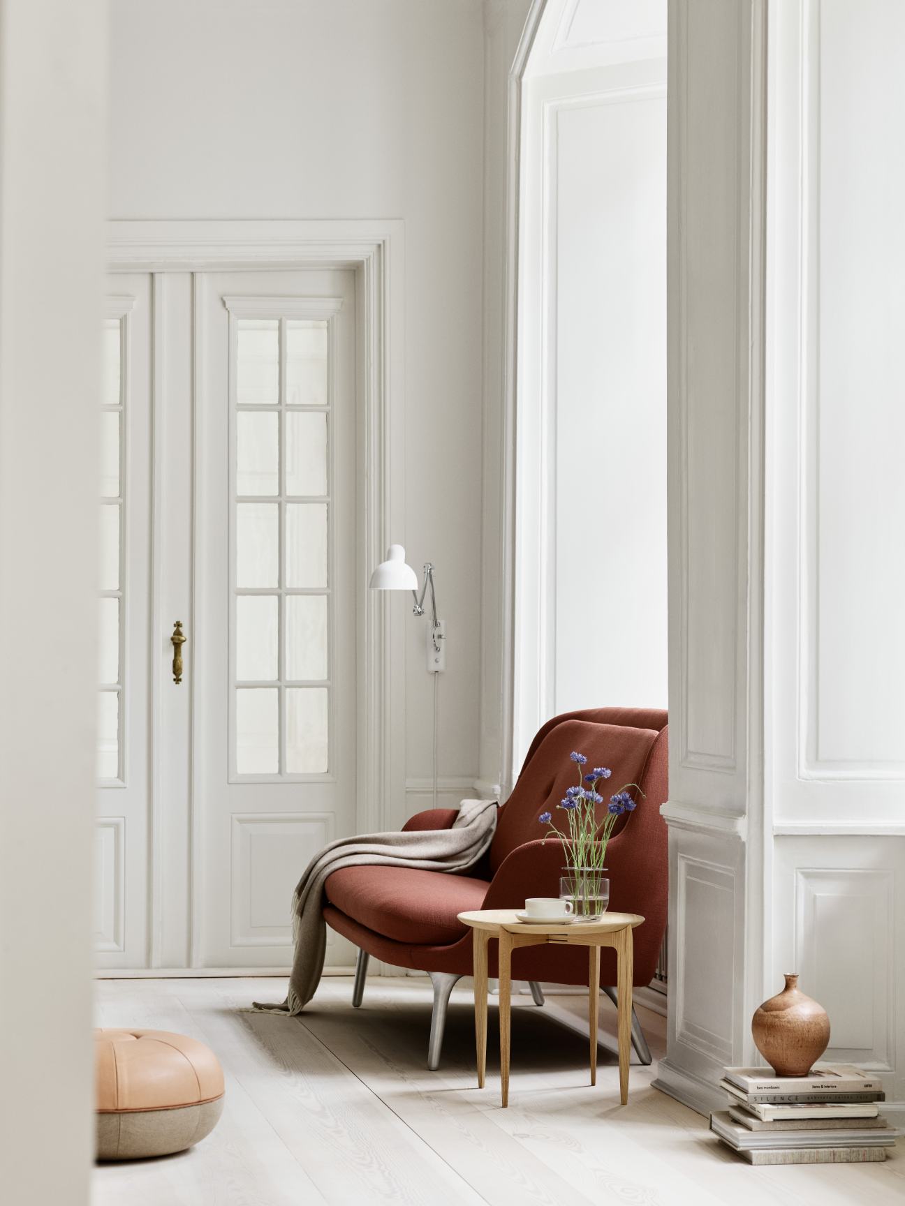 Wohnzimmer Interieur mit rotem Sessel, Beistelltisch und Fritz Hansen Pouf Small Hocker aus Leder.