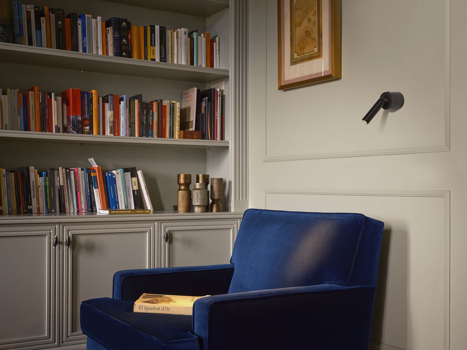 Ledtube A Wandleuchte von Marset in Schwarz, neben einem Sessel und Bücherregal.