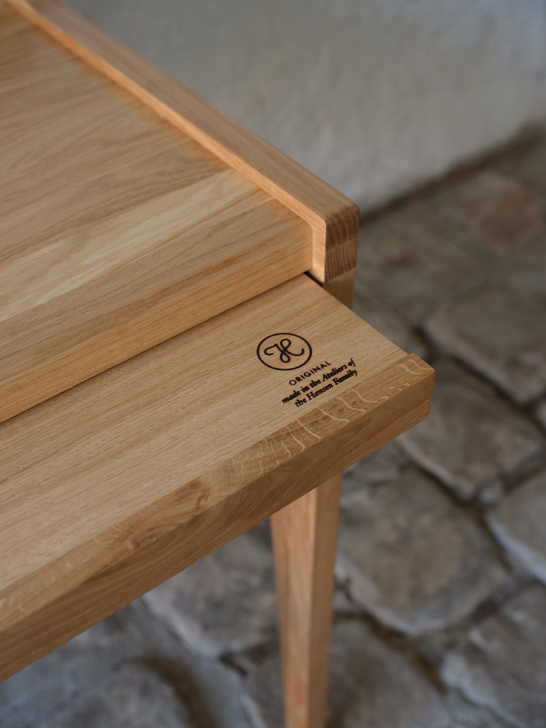 Detailaufnahme des The Hansen Family Schreibtischs aus hellem Holz mit Logo und feiner Maserung.