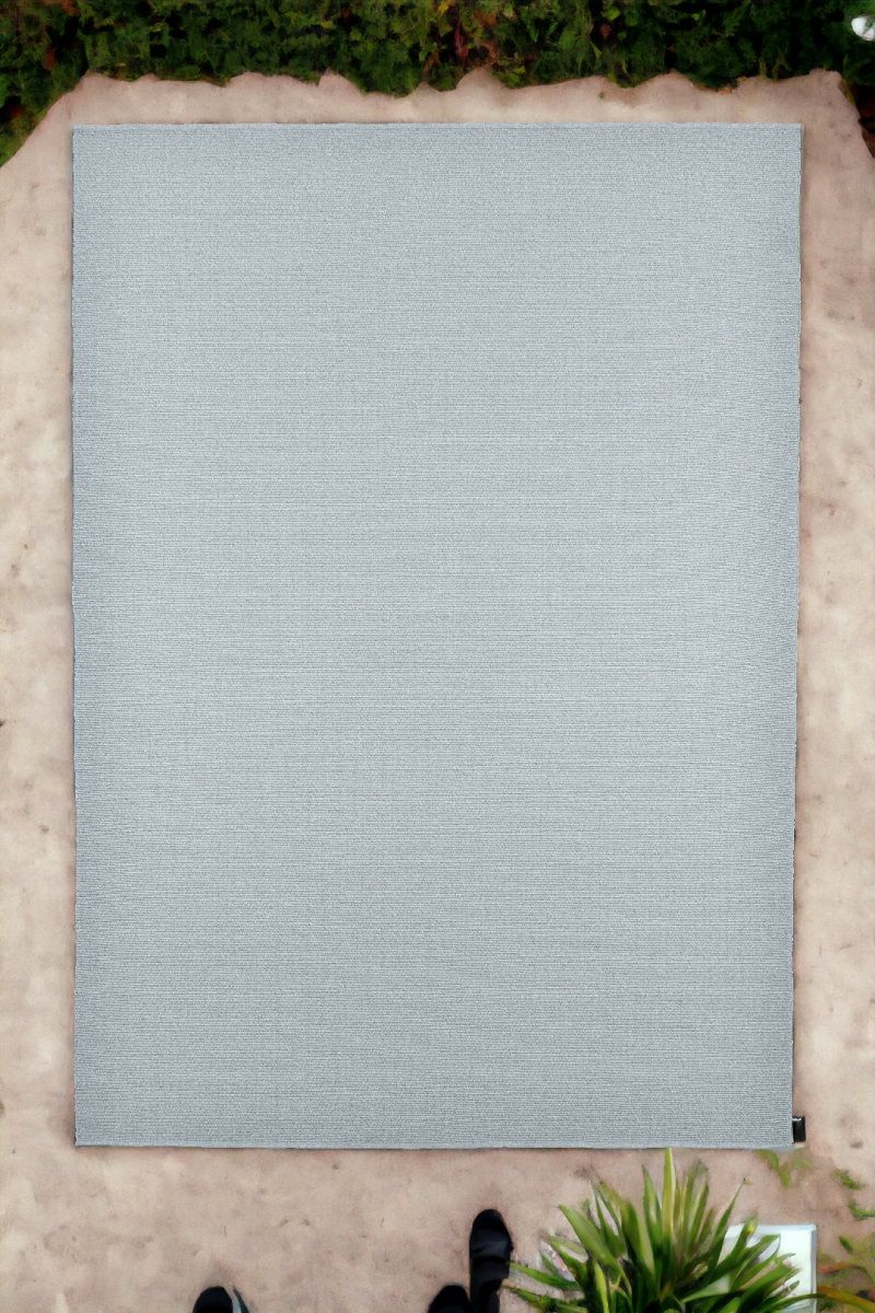 Grauer Koi Outdoor Teppich von miinu auf einer Terrasse, umgeben von Pflanzen.