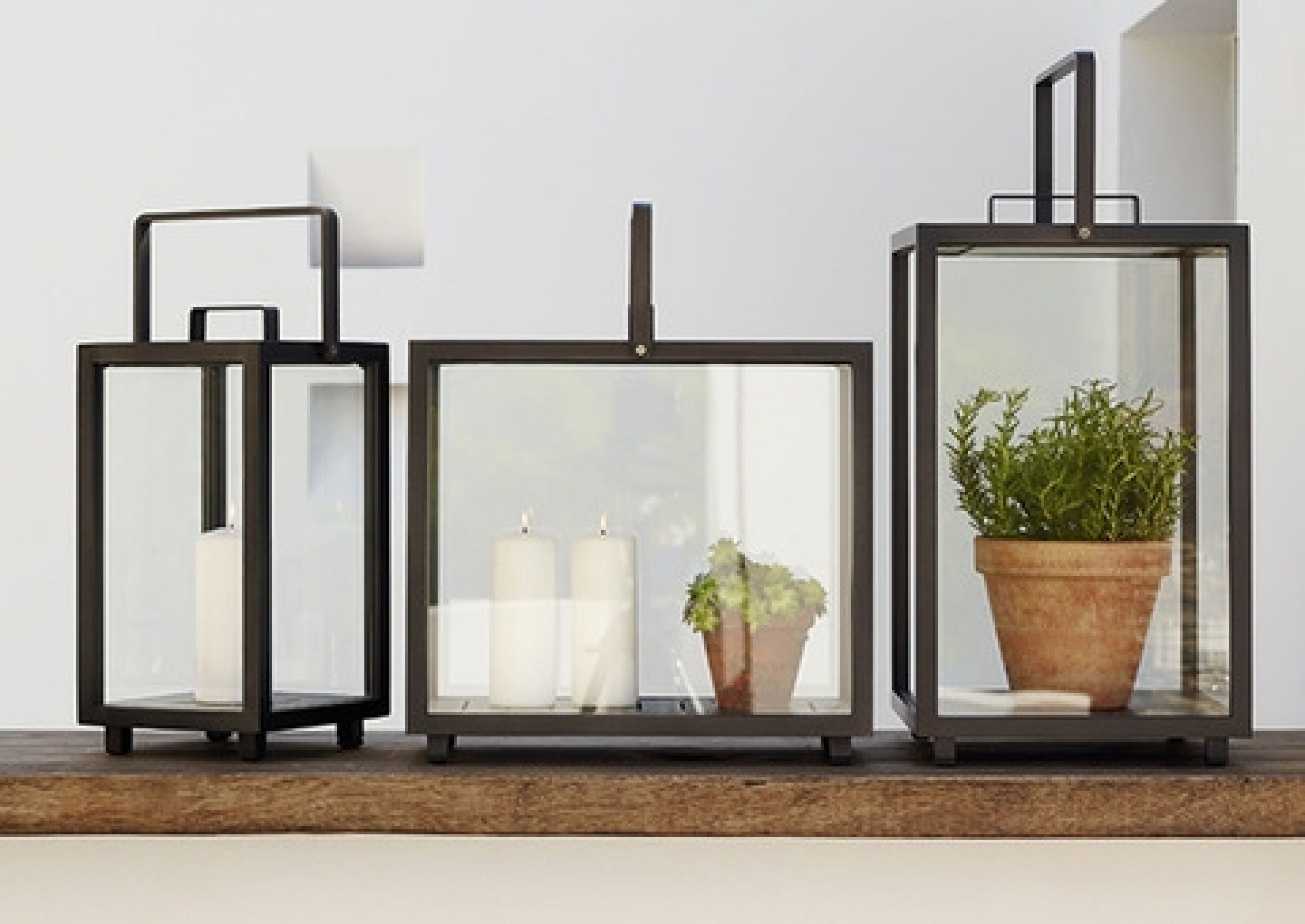 Drei Cane-Line Lighthouse Laternen aus Aluminium mit Kerzen und Pflanzen auf einem Holztisch.