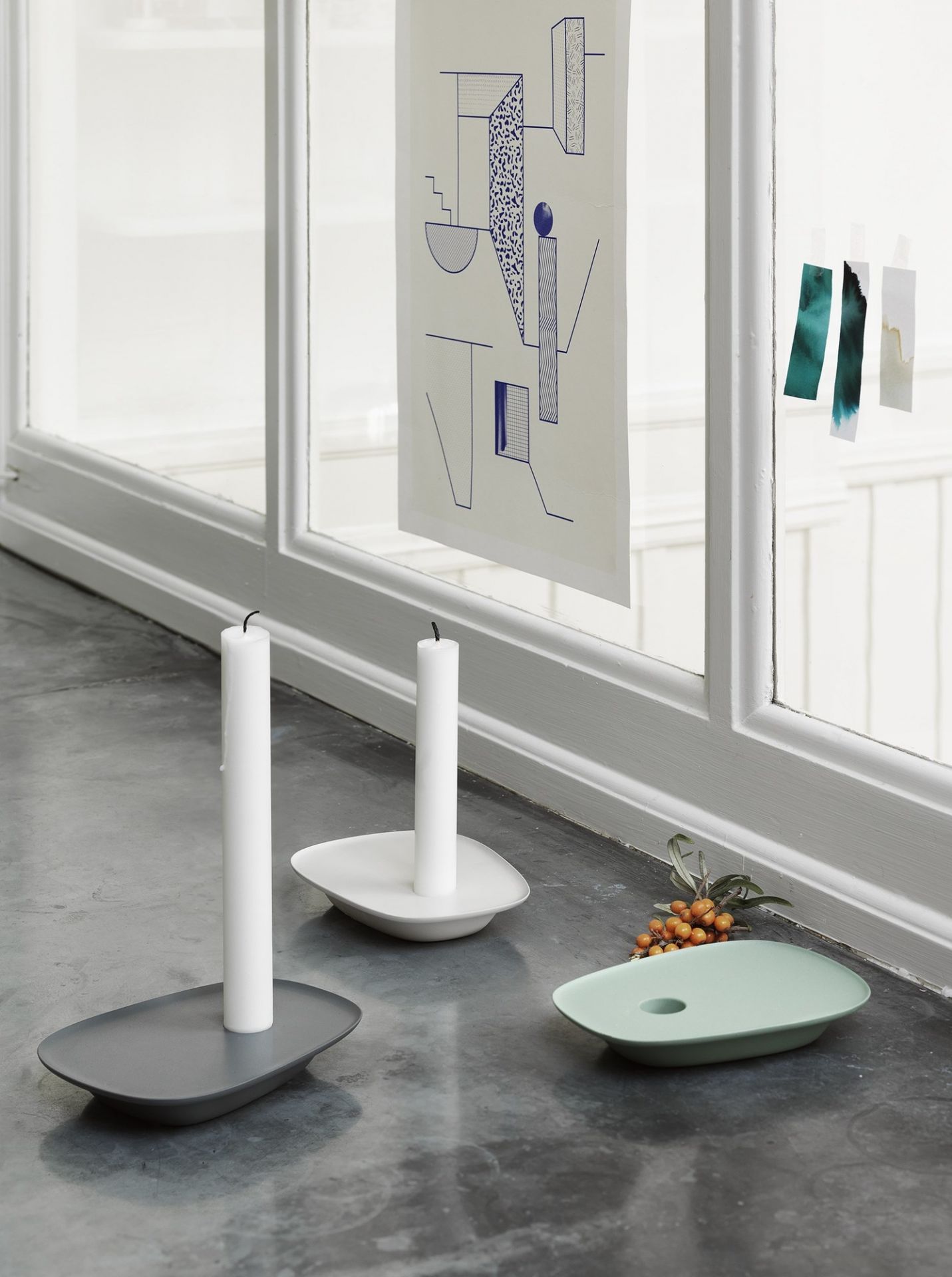 Drei Muuto Float Kerzenhalter in Grau, Weiß und Mintgrün mit weißen Kerzen.