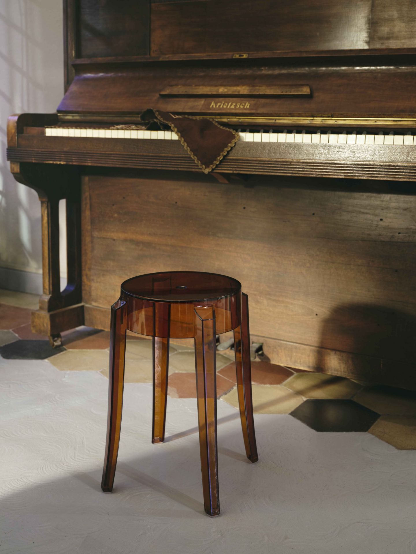 Brauner Charles Ghost Hocker von Kartell vor einem Klavier. Design Hocker für Wohnzimmer.