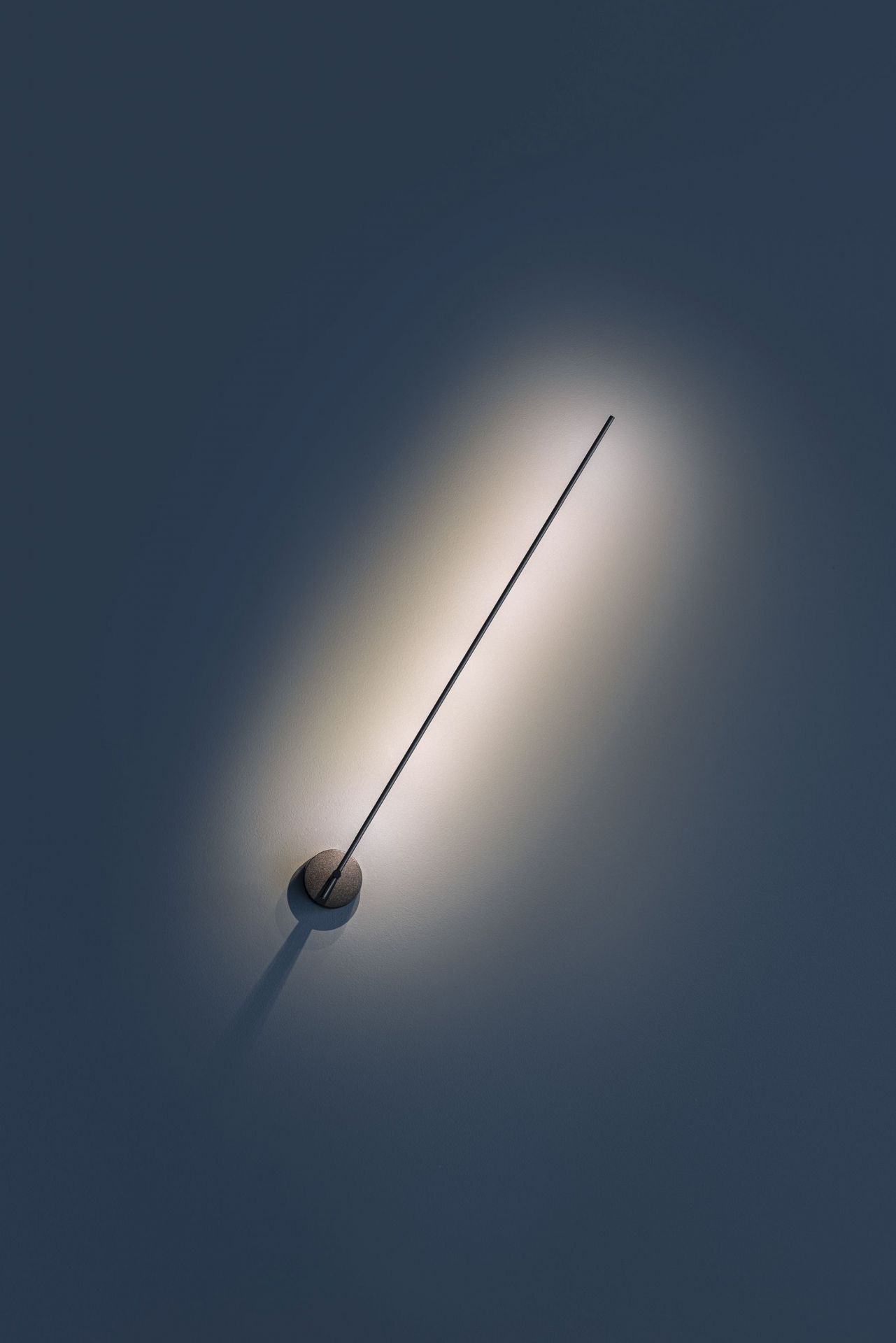Light Stick Wandleuchte von Catellani & Smith, modernes Design mit warmem Lichtkegel an dunkler Wand.