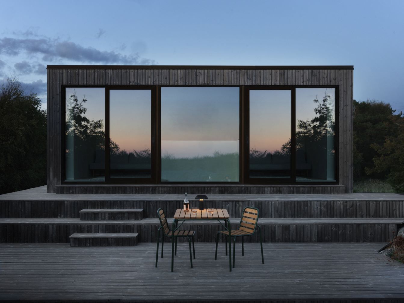 Vig Table von Normann Copenhagen: Quadratischer Outdoor-Tisch aus Holz mit zwei Stühlen auf Holzterrasse.