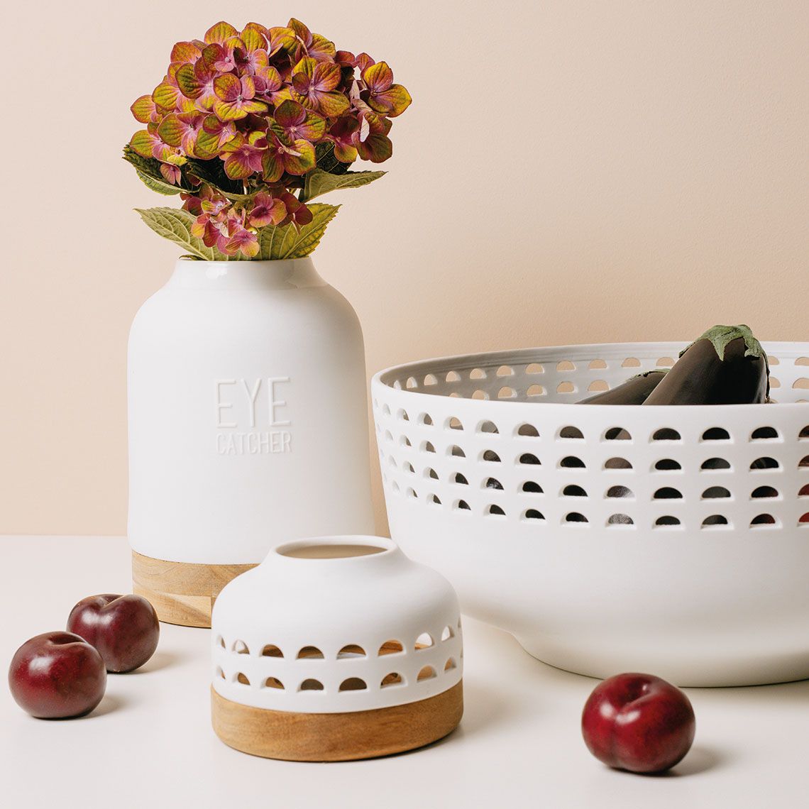 Weiße Eyecatcher Vase von Räder mit Blumen, dekorative Schale und Pflaumen auf hellem Untergrund.