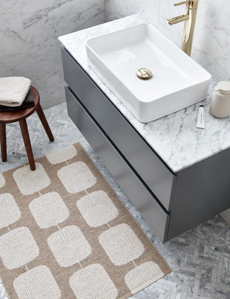 Sten Kunststoffteppich in Army/Fossil Grau (Pappelina) im Badezimmer, neben einem grauen Waschtisch.