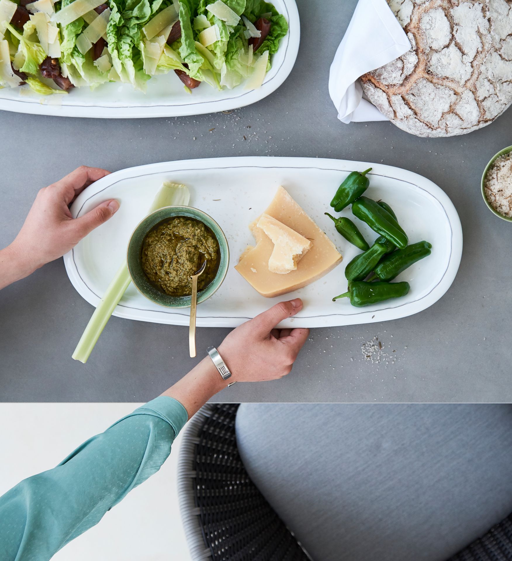 Pure Outdoor Esstisch: Detailaufnahme mit Speisen wie Salat, Pesto, Käse und Brot auf grauem Tisch.
