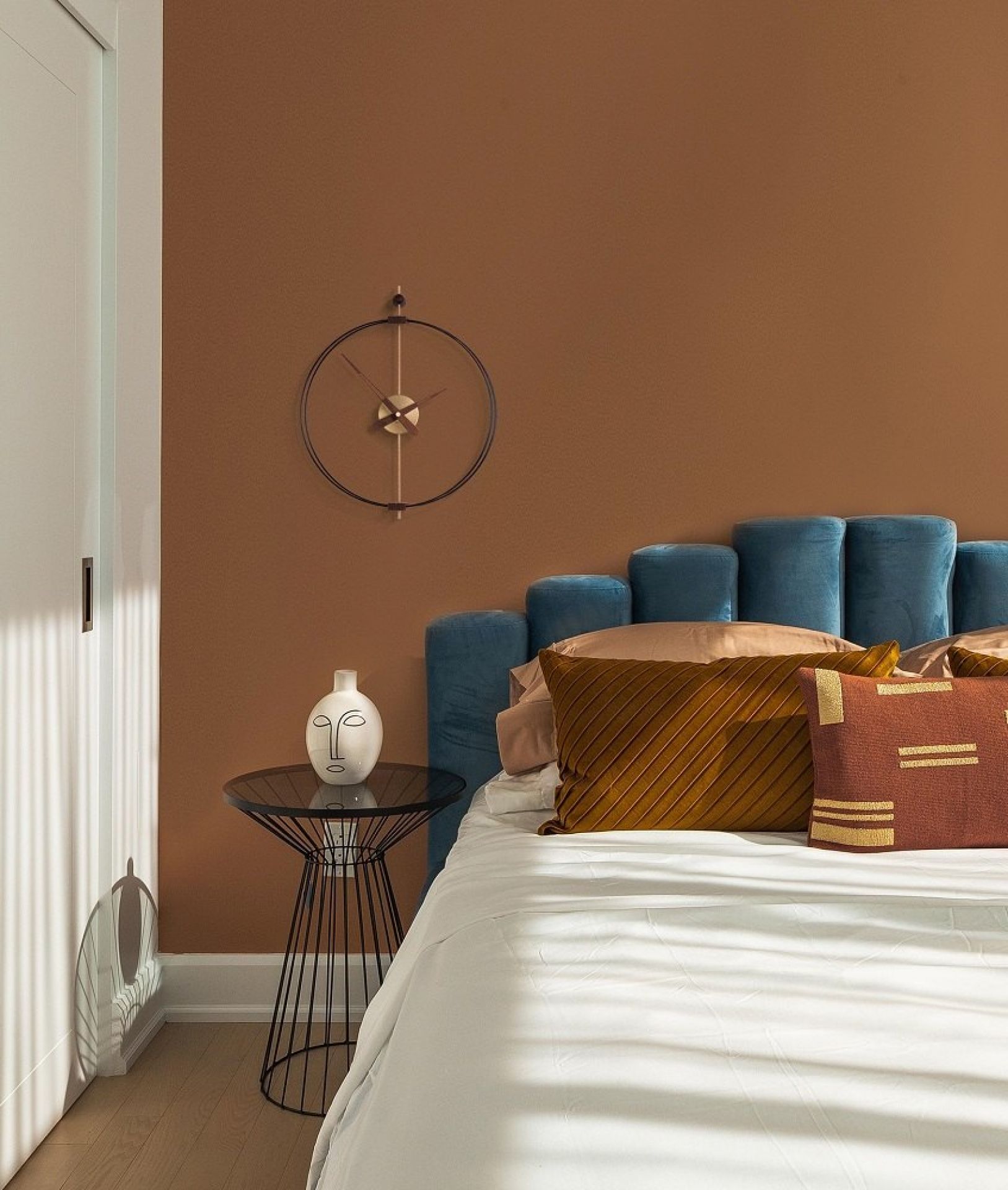 Schwarze Micro Barcelona Clock Wanduhr von nomon an brauner Wand über einem Bett im Schlafzimmer.