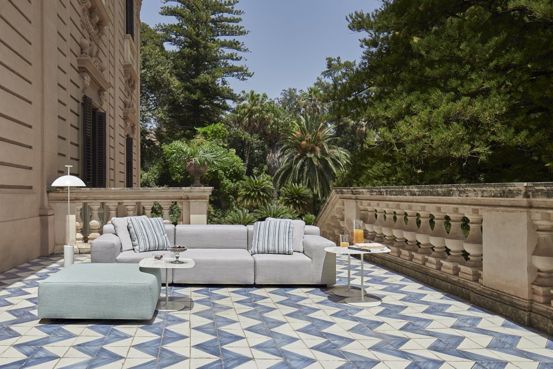 Graues Kartell Outdoor Sofa mit Kissen und Hocker auf einer Terrasse mit blau-weißen Fliesen.