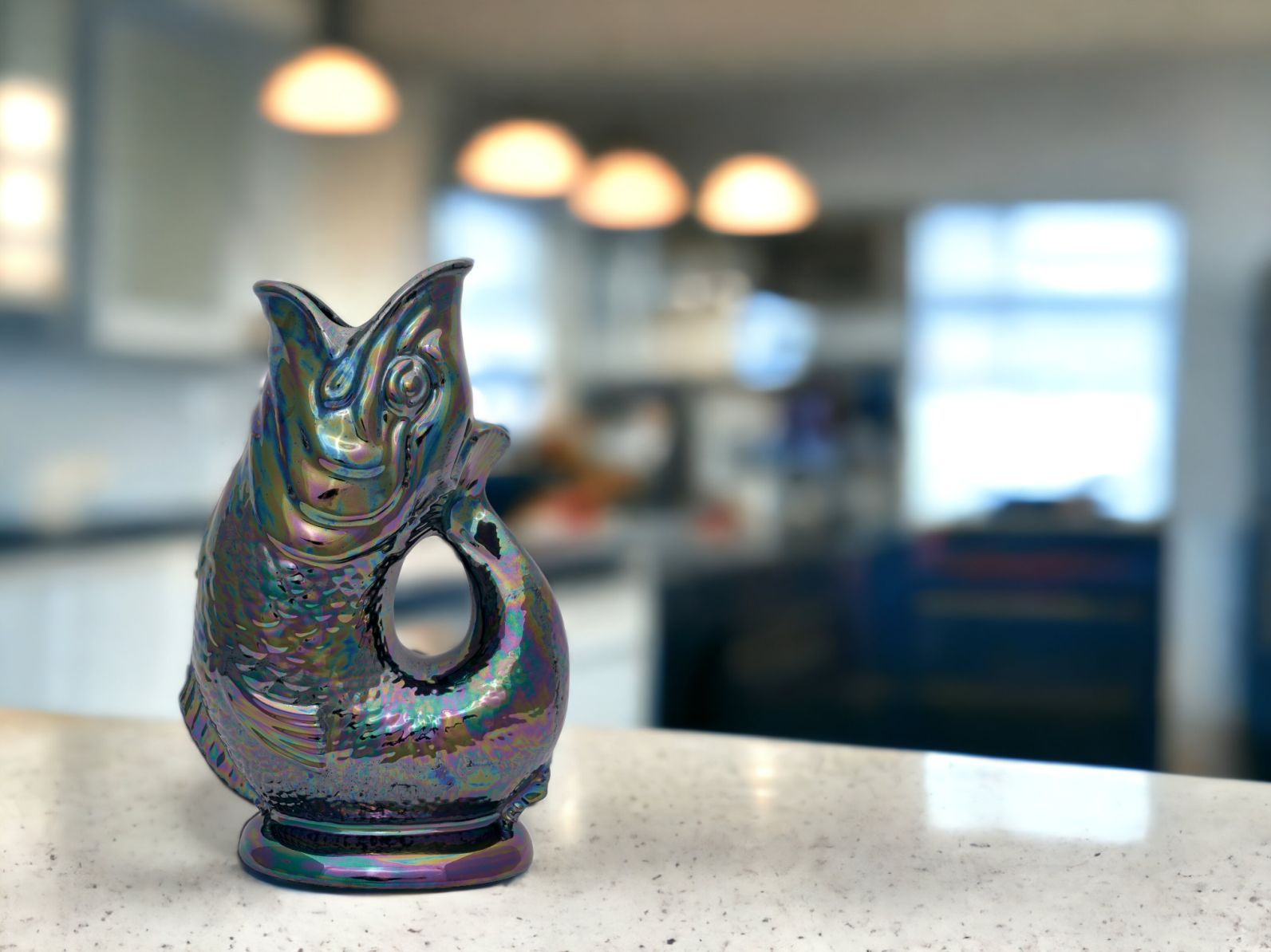 Gluckigluck Karaffe in Fischform, schillernd, auf einer Küchentheke. Dekorative Wasserkaraffe für den Esstisch.