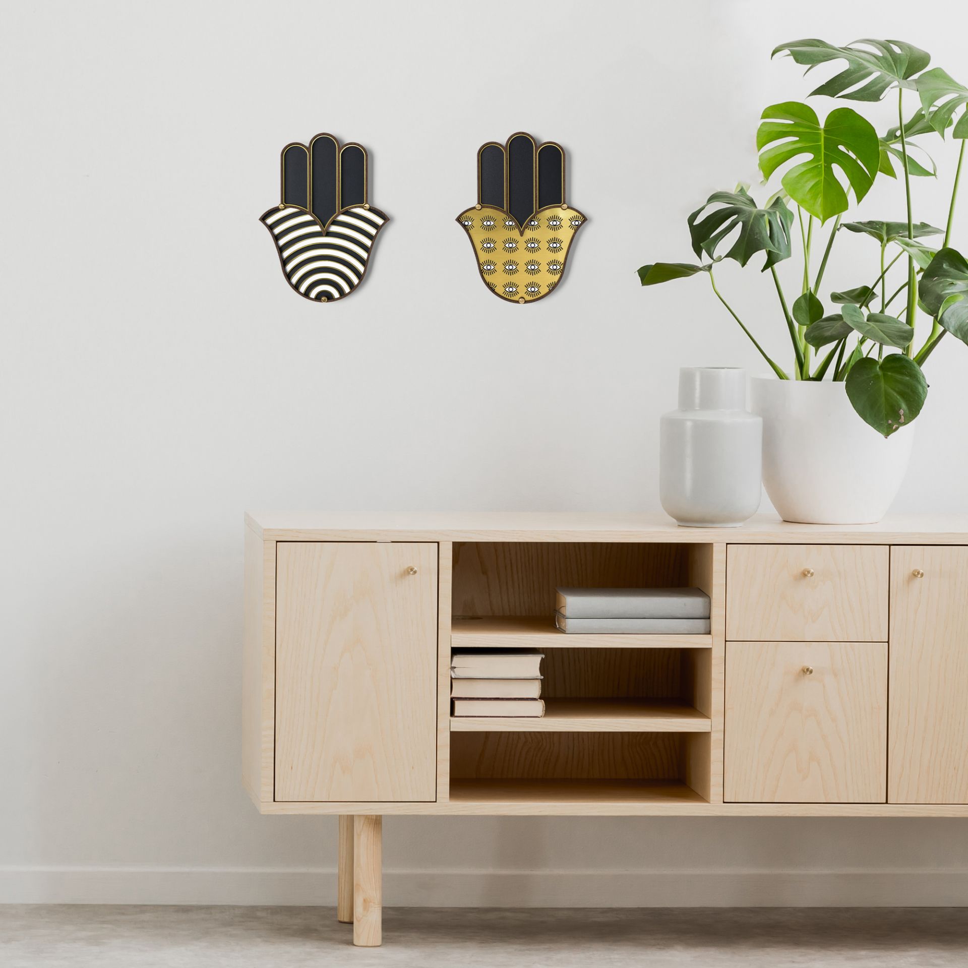 Zwei Hamsa Wandschmuck-Dekorationen von Umasqu an einer weißen Wand über einem hellen Holzschrank.