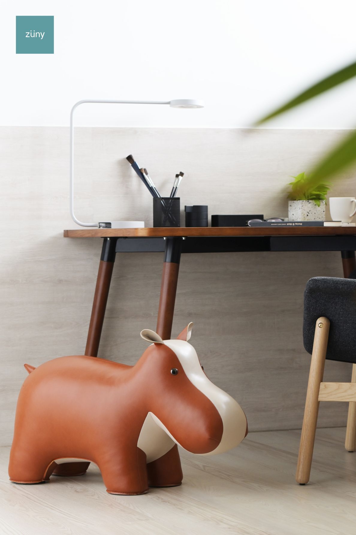 Brauner Hippo Hocker Züny aus Kunstleder vor einem Schreibtisch im modernen Büro.