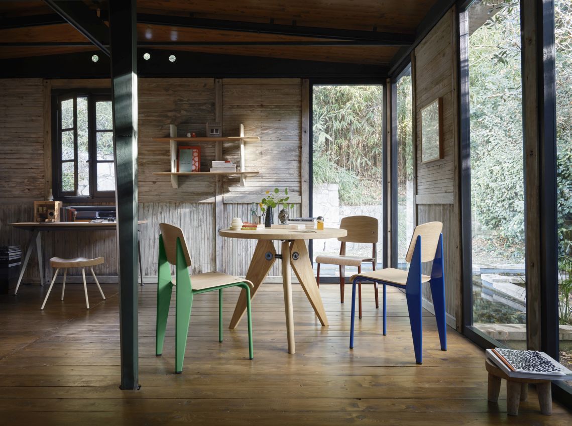 Innenaufnahme mit Vitra Wandregal aus Eiche und farbigen Stühlen. Modernes Design für Wohnzimmer und Büro.