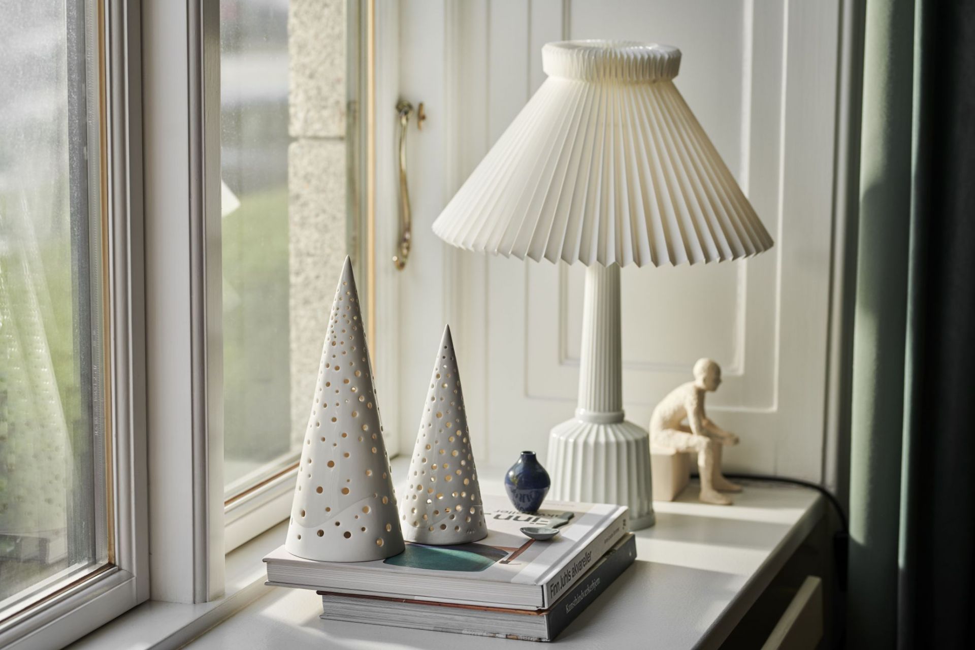 Zwei schneeweiße Nobili Teelichthalter von Kähler in Kegelform mit Lochmuster auf Büchern.