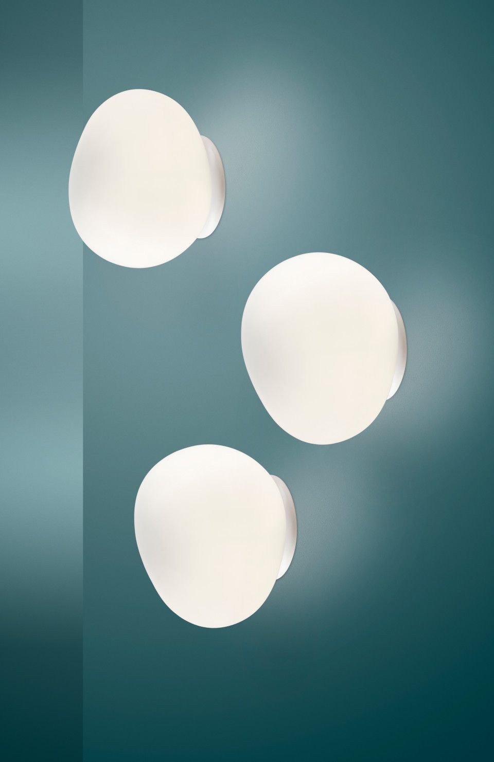 Drei leuchtende Gregg Wandleuchten von Foscarini an einer türkisfarbenen Wand, modernes Design.