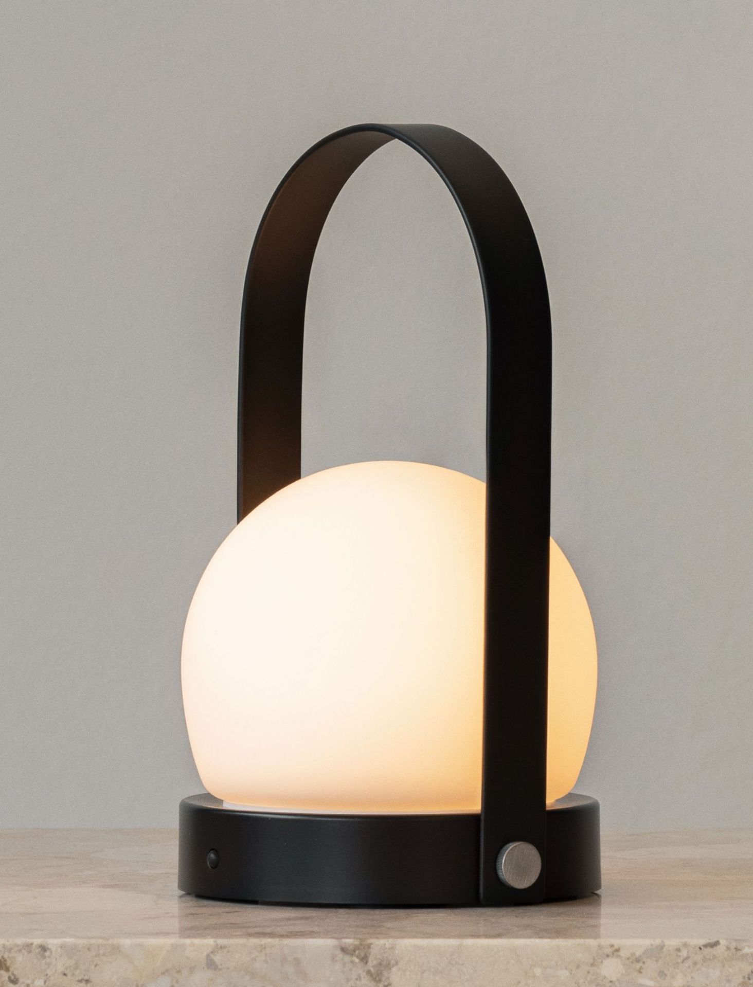 Carrie tragbare Tischleuchte: Akkuleuchte mit schwarzem Tragegriff und warmweißem Licht auf einem Tisch.