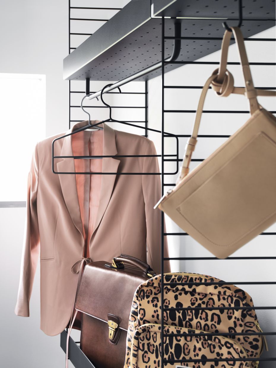 String Furniture Kleiderbügel: Blazer, Aktentasche und Taschen hängen an einem schwarzen Design-Kleiderbügel.